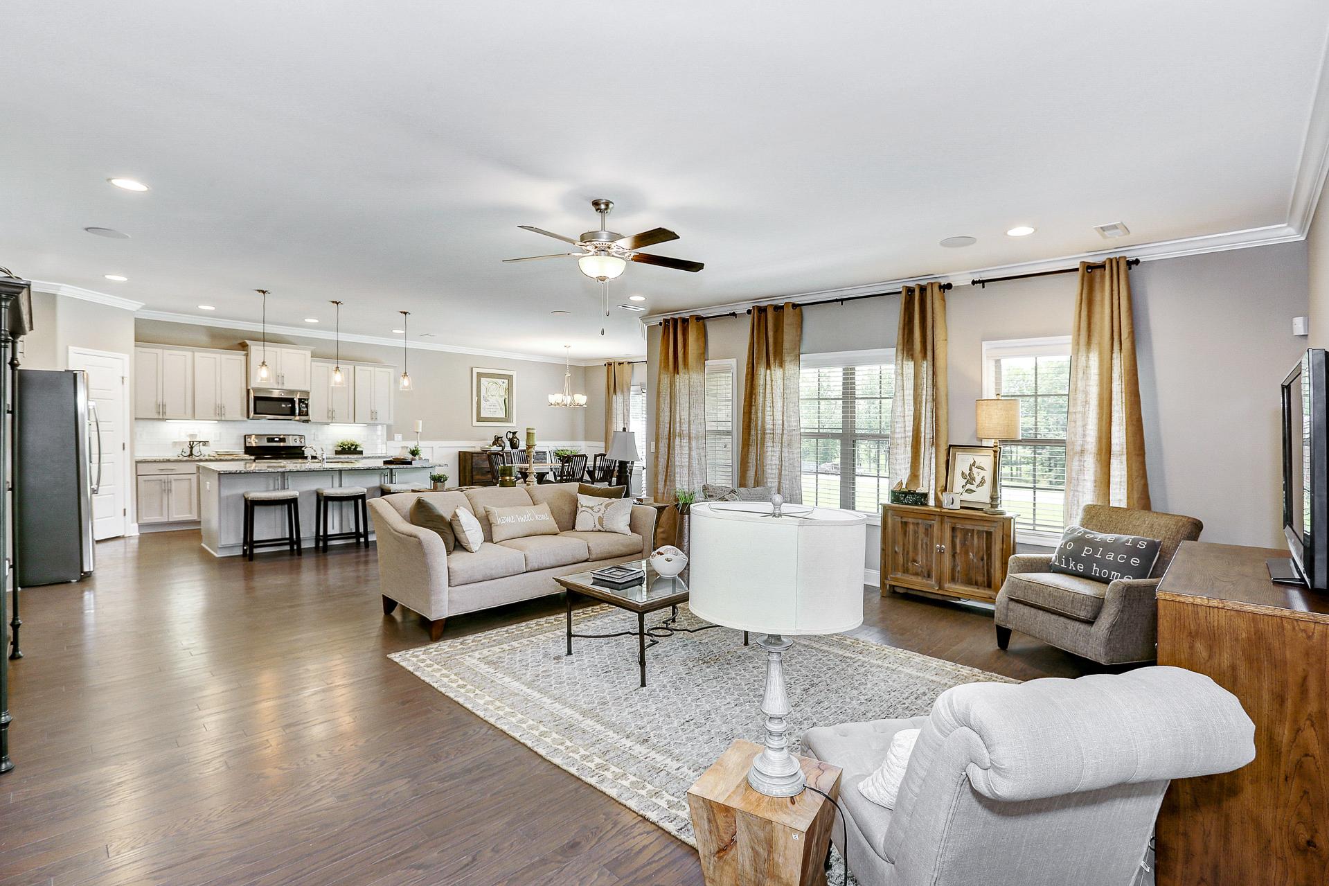 Open-concept living room and kitchen in Stone Creek Phase II Cullman Alabama with hardwood floors, beige sofa, and large windows