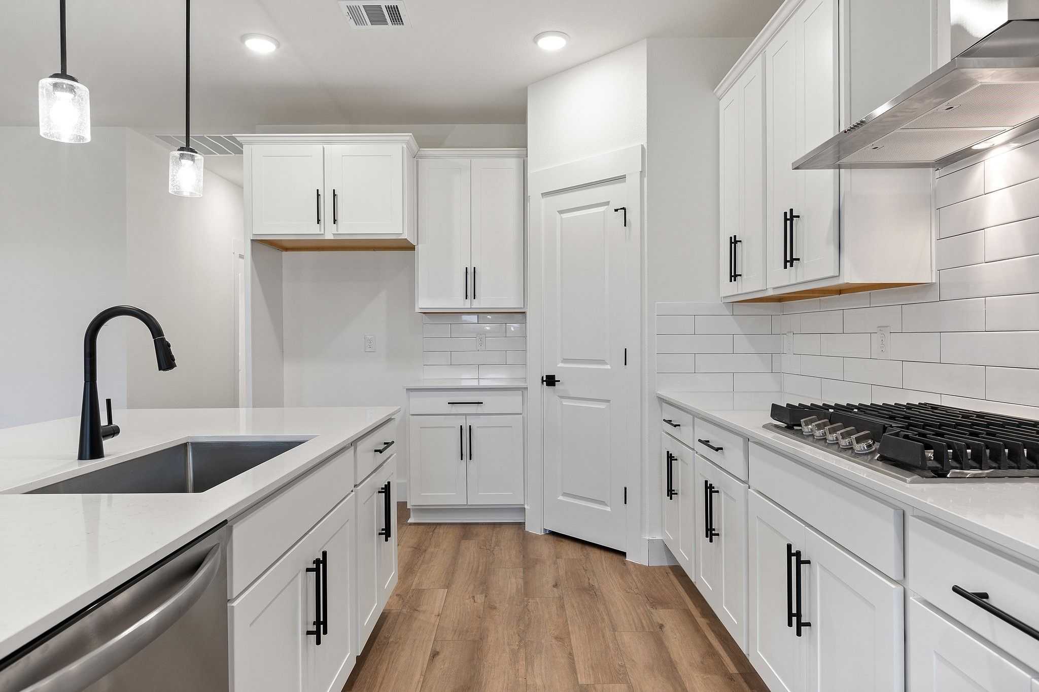 Modern white kitchen with large island, black faucet, subway tile backsplash, and stainless appliances in The Rockford C by Davidson Homes, Josephine, Texas