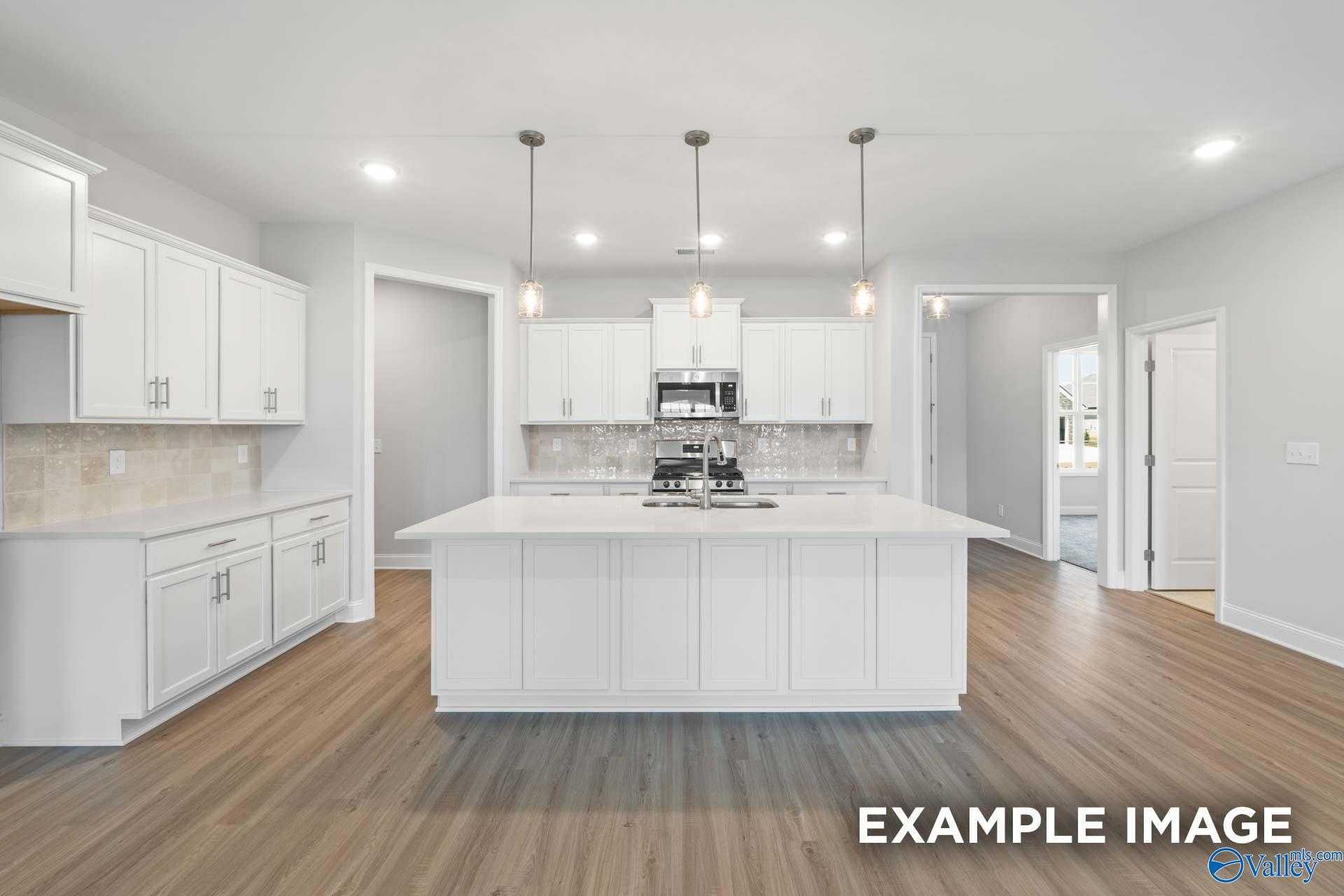 Modern white kitchen with large island, stainless appliances, pendant lights, and open layout in The Lanier by Davidson Homes, Meridianville, AL
