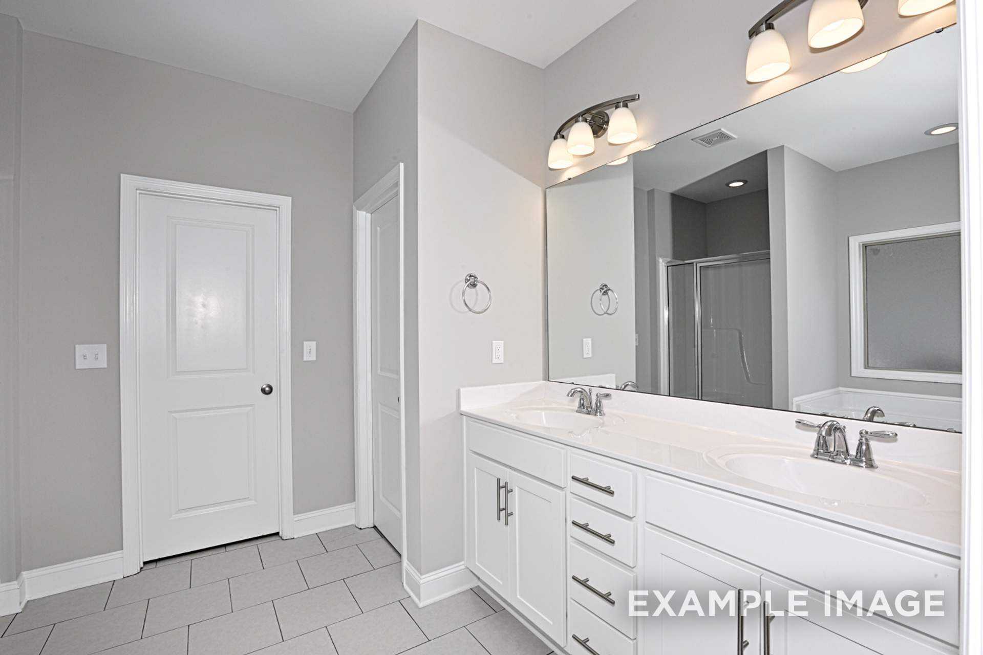 Spacious master bathroom in The Montgomery C featuring double vanity, frameless glass shower, and neutral gray tones