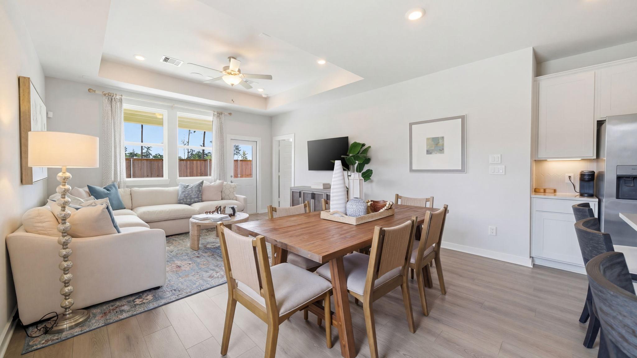 Open-concept living room and kitchen at Spring Branch Crossing in Conroe Texas featuring pink armchairs, hardwood floors, and white cabinetry
