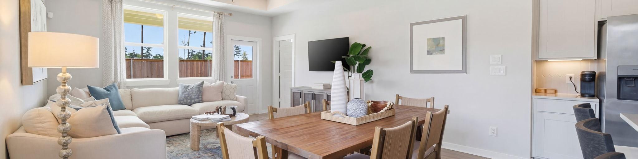 Open-concept living room and kitchen at Spring Branch Crossing in Conroe Texas featuring pink armchairs, hardwood floors, and white cabinetry