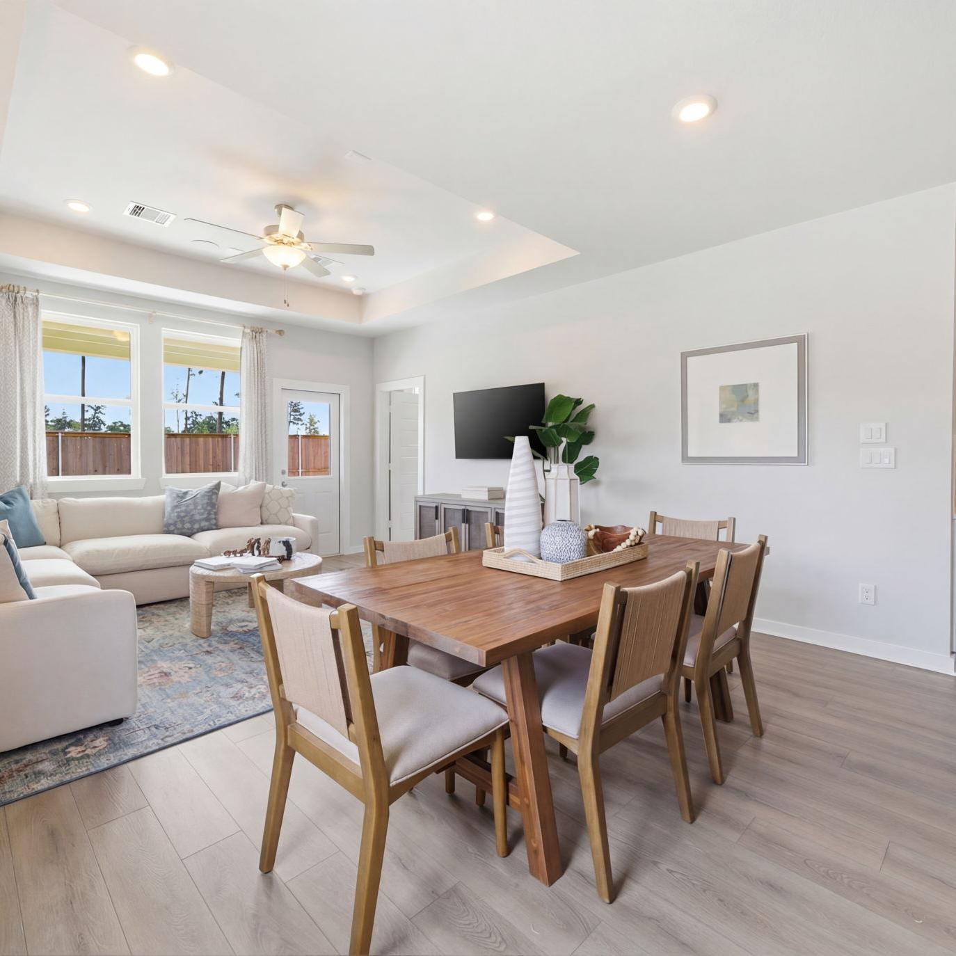 Open-concept living room and kitchen at Spring Branch Crossing in Conroe Texas featuring pink armchairs, hardwood floors, and white cabinetry