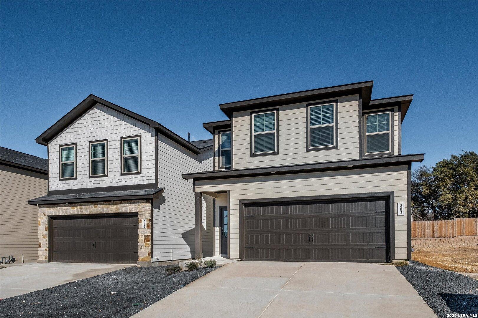 Modern two-story Charlotte A home with beige siding, stone accents, two-car garage, and driveway in Meadows at Oak Creek, San Antonio, Texas