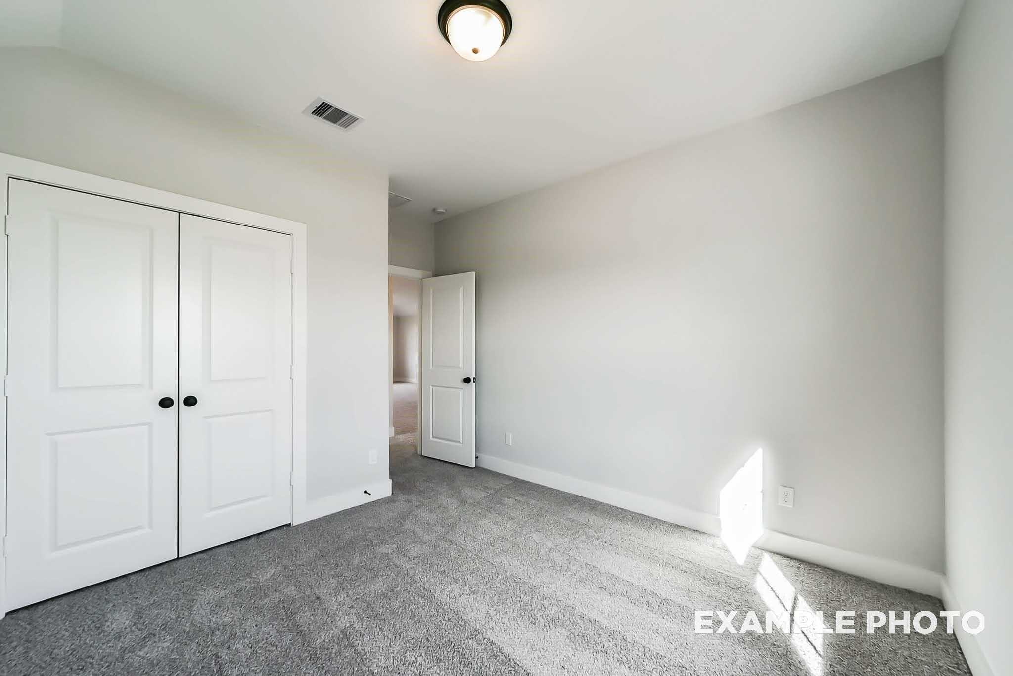 Bright bedroom with gray carpet, white double closet doors, and soft natural light in Davidson Homes The Philip C, Rosharon, Texas