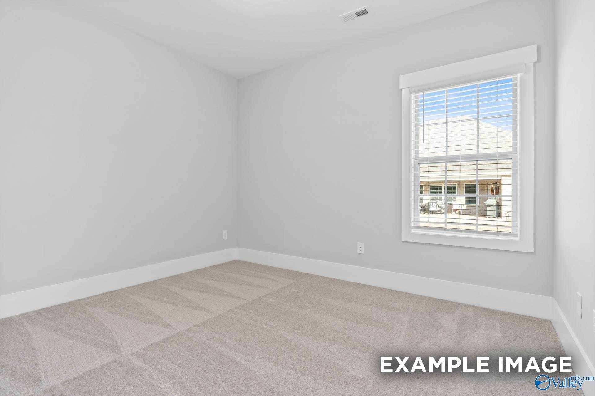 Empty secondary bedroom featuring light gray walls, neutral carpet, and large window in Davidson Homes The Rockford, Meridianville, Alabama