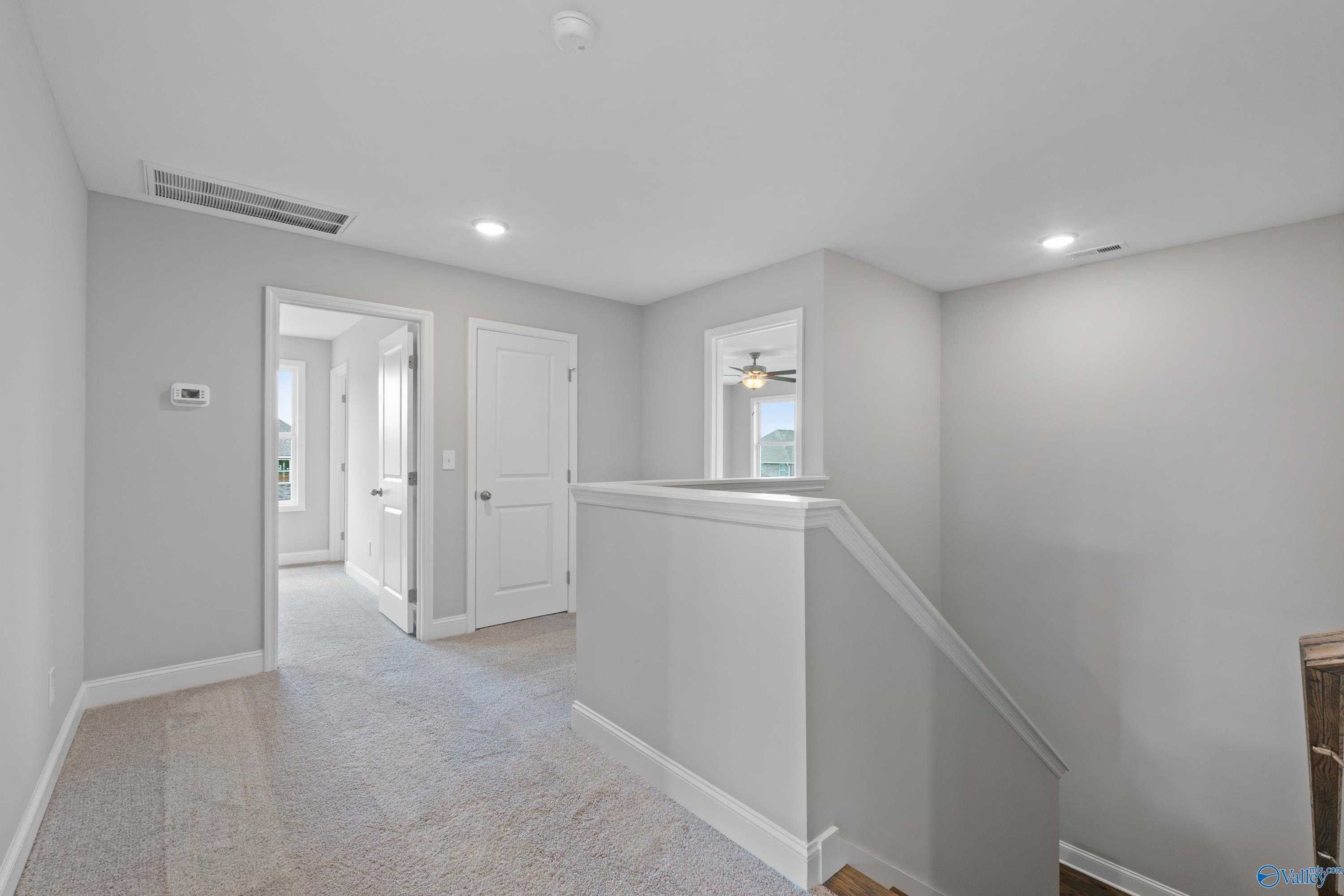 Spacious upstairs hallway with gray walls, carpeted floors, bedroom doors, and staircase in 5-bedroom The Chelsea B home, New Market, Alabama