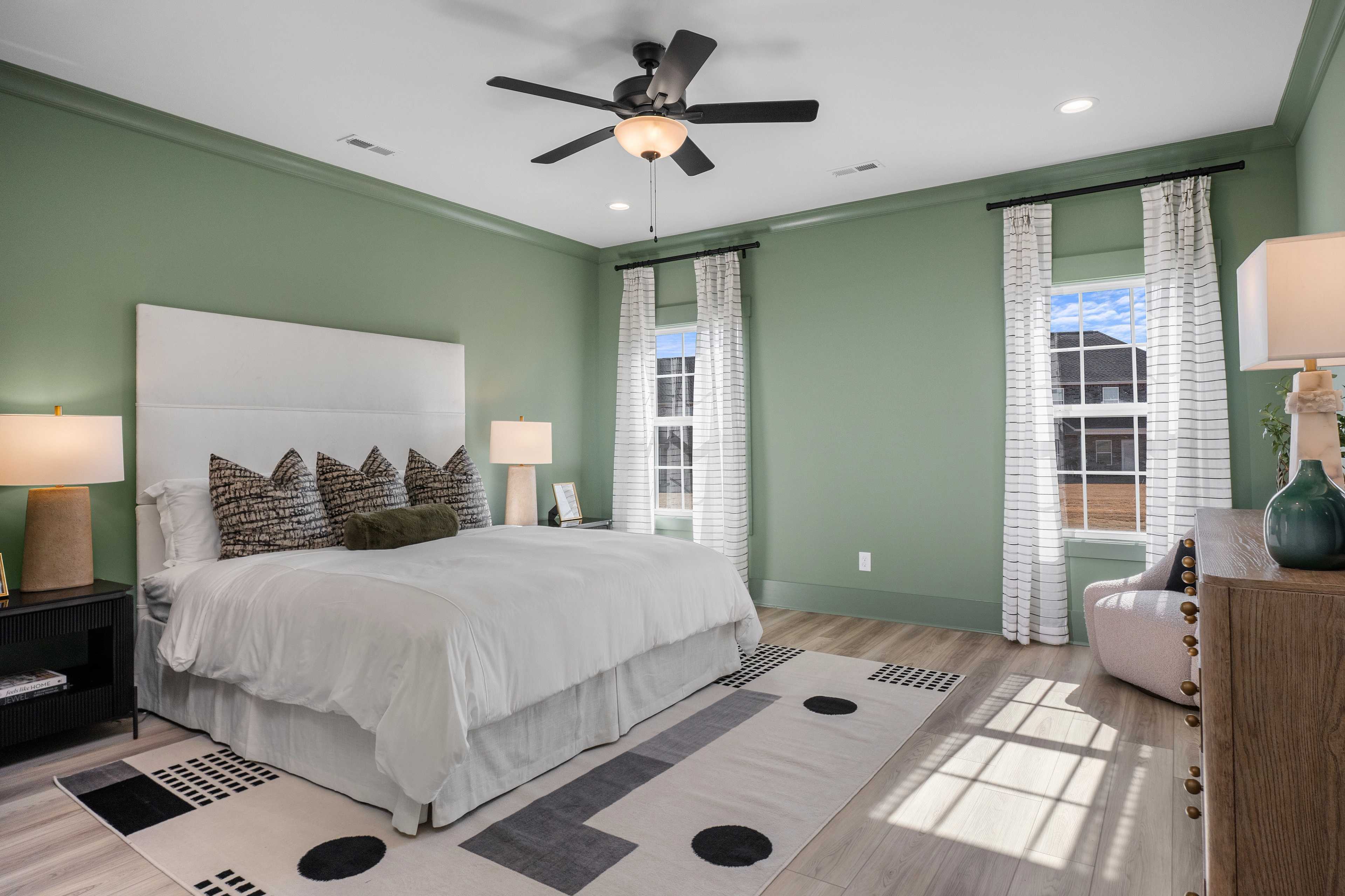 Elegant master bedroom at Barnett's Crossing Madison AL with sage green walls, king bed, ceiling fan, and hardwood floors
