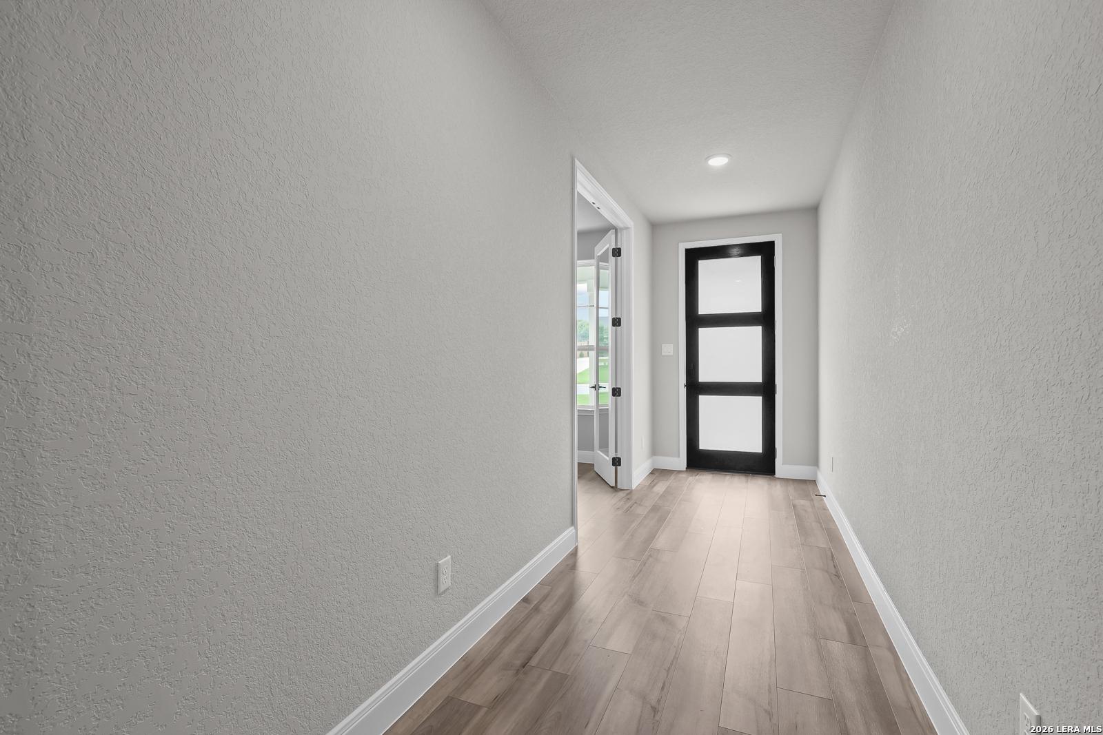 Bright hallway featuring light gray walls, hardwood floors, and black glass door in The Belmont H home, Castroville, Texas