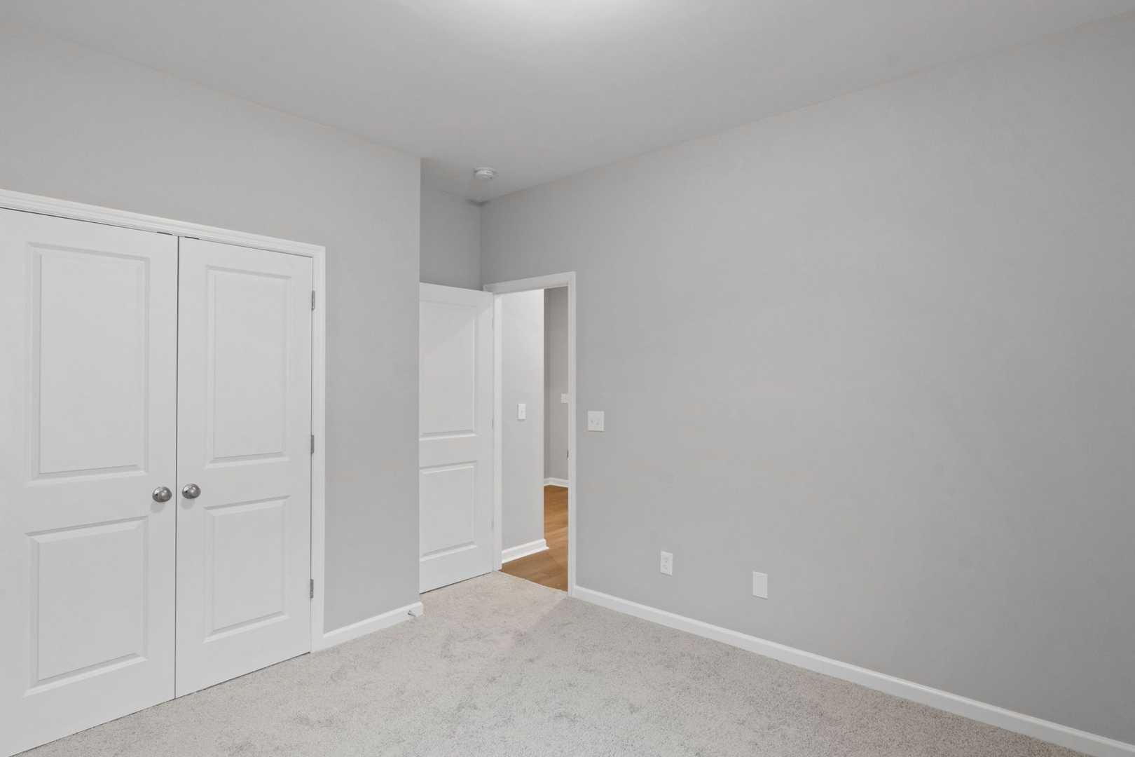 Spacious master bedroom in The Luna with light gray walls, white double closet doors, and open bathroom doorway