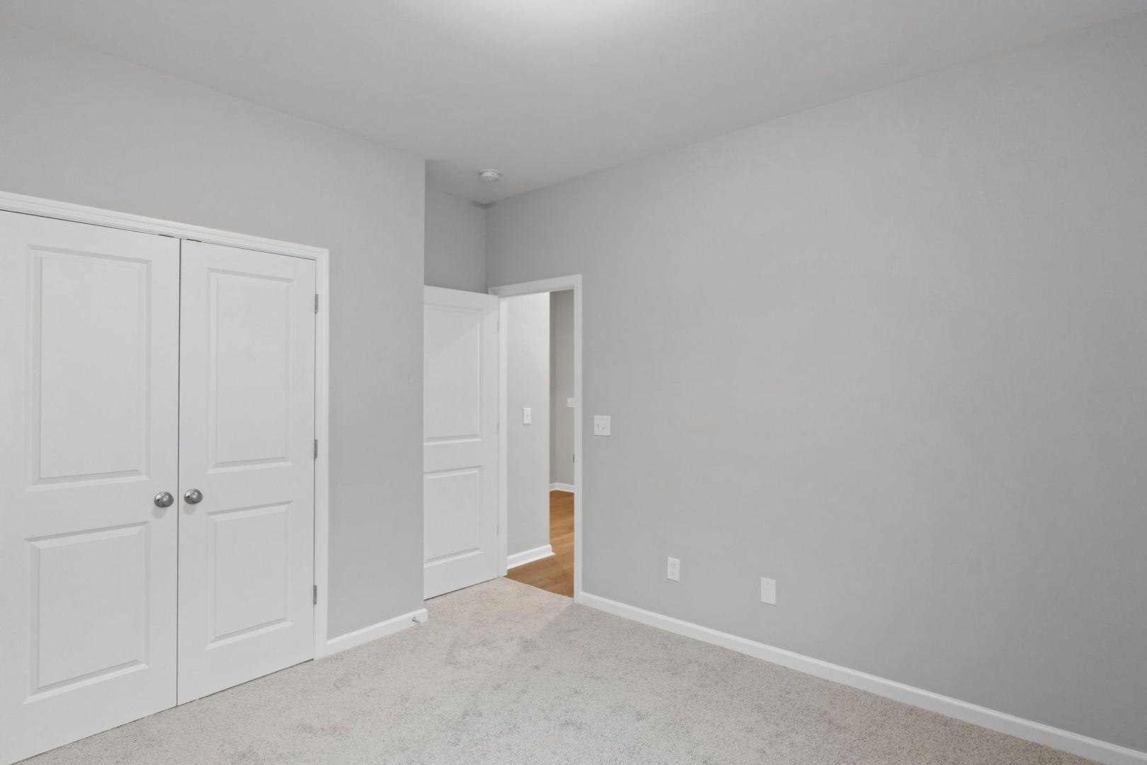 Spacious master bedroom in The Luna with light gray walls, white double closet doors, and open bathroom doorway