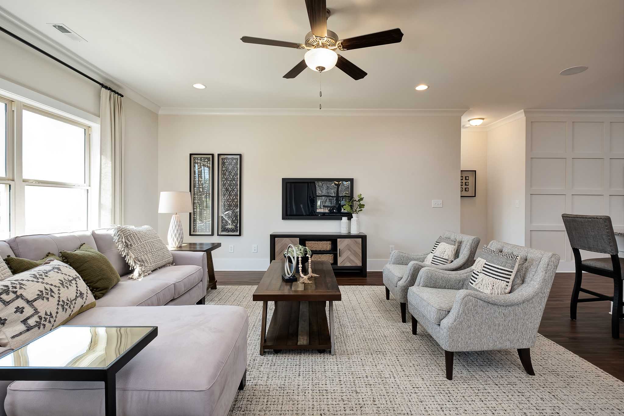 Open-concept living room in Magnolia Preserve Hartselle AL with gray sectional sofa, accent chairs, hardwood floors, and ceiling fan