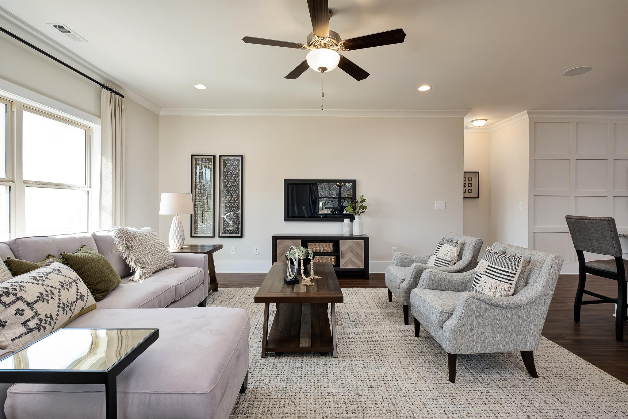 Open-concept living room in Magnolia Preserve Hartselle AL with gray sectional sofa, accent chairs, hardwood floors, and ceiling fan