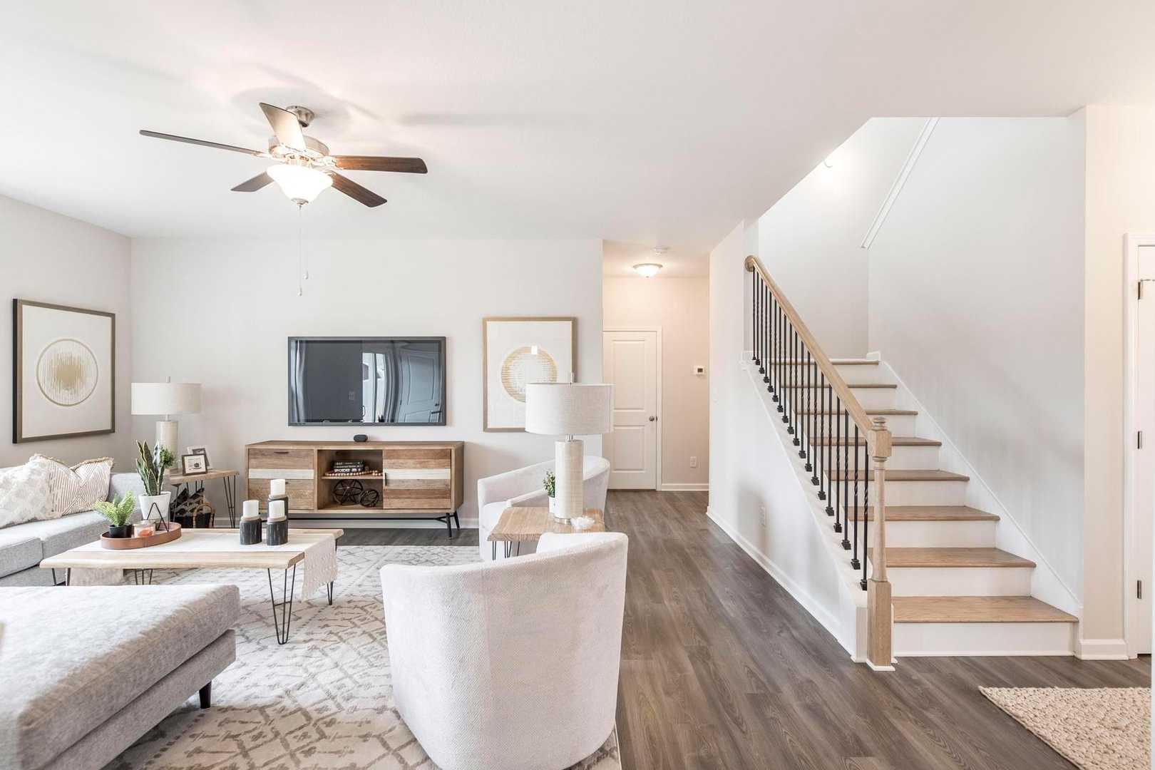 Spacious open-concept living room at Cape Reserve Donahue Ridge in Auburn Alabama with gray sectional sofa, TV console, hardwood floors, and staircase