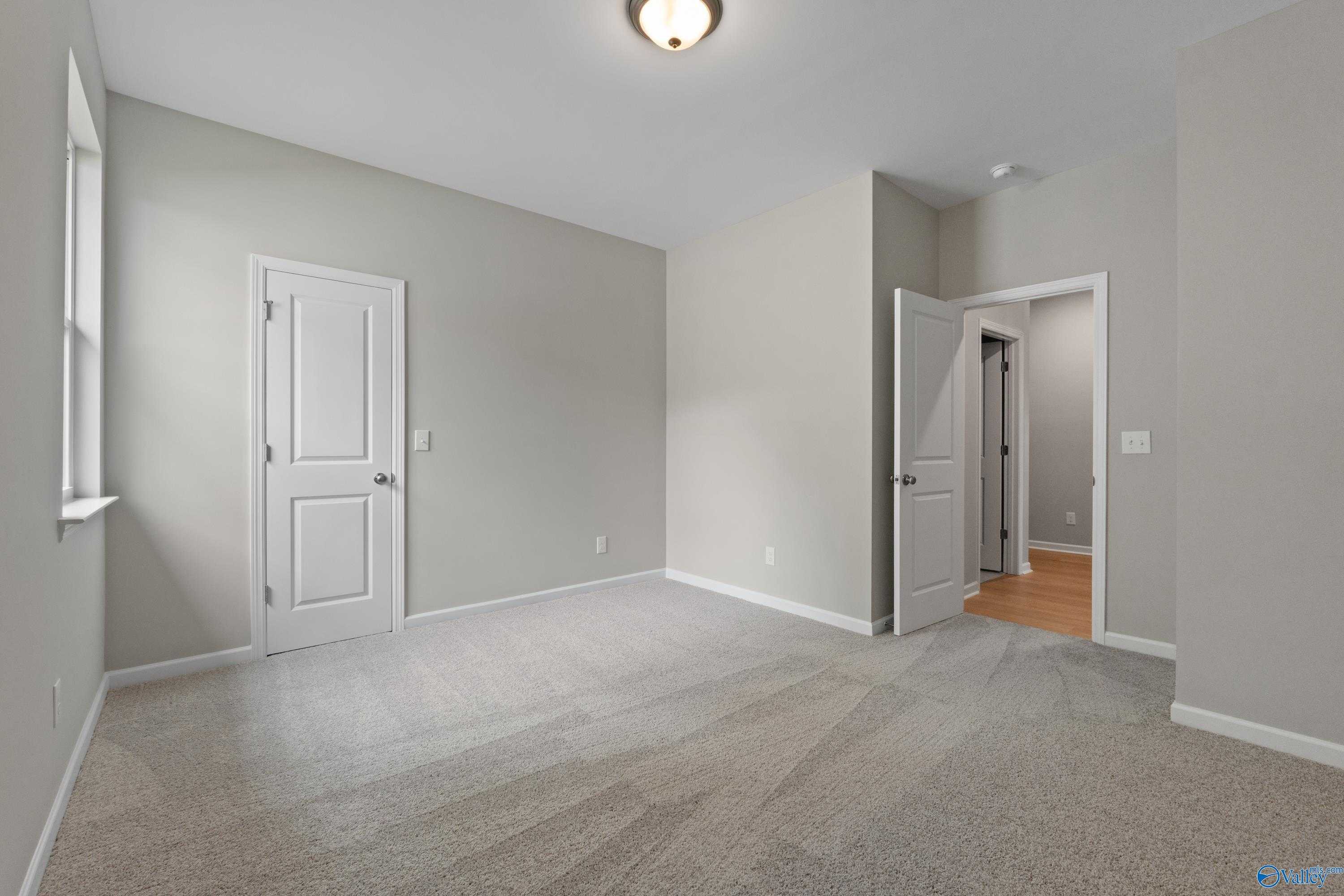 Spacious empty bedroom with light gray walls, plush carpet, double closet doors, and bathroom access in Davidson Homes The Luna, Hazel Green