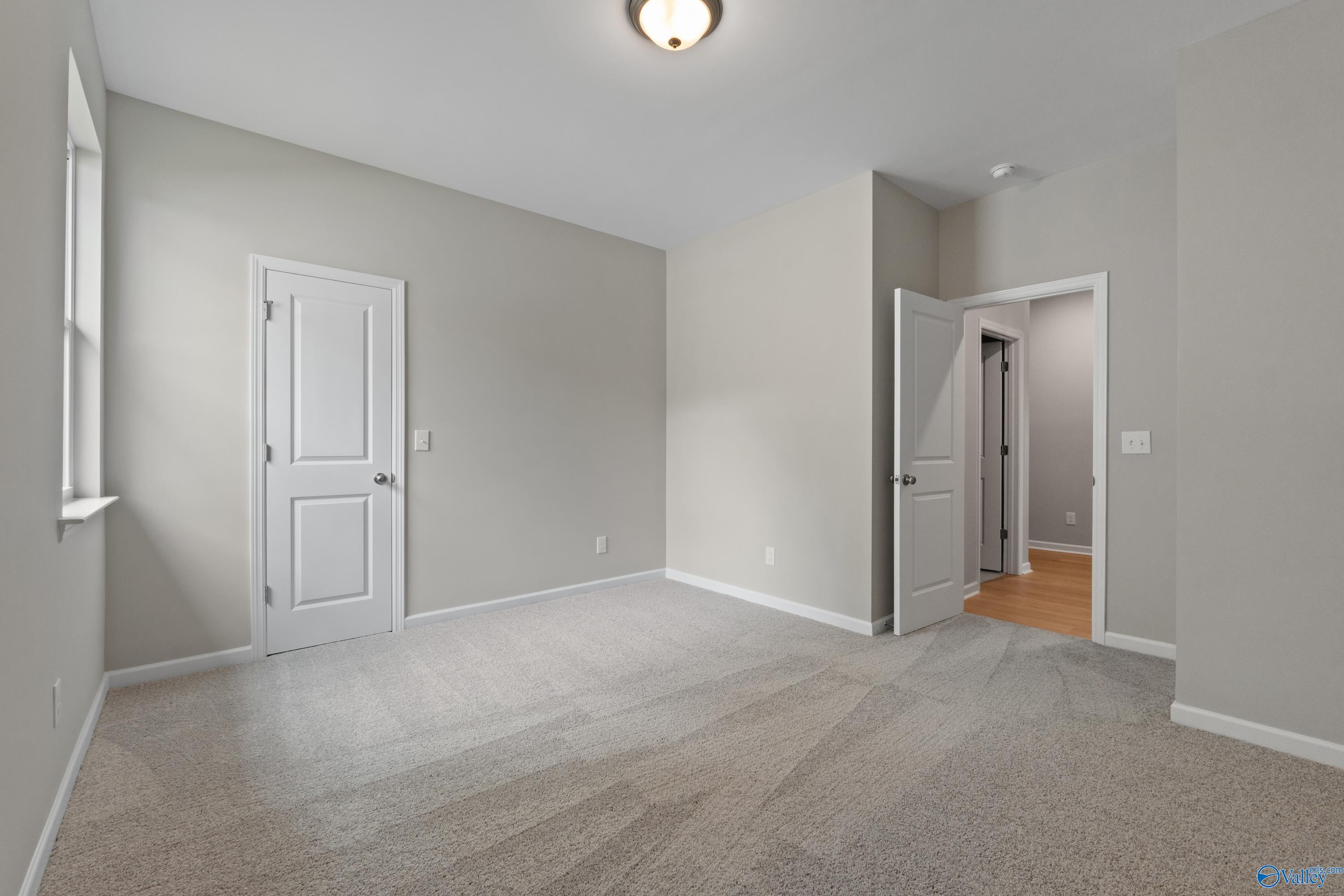 Spacious empty bedroom with neutral gray walls, white doors, and carpet flooring in The Luna 4-bedroom home, Hazel Green, Alabama