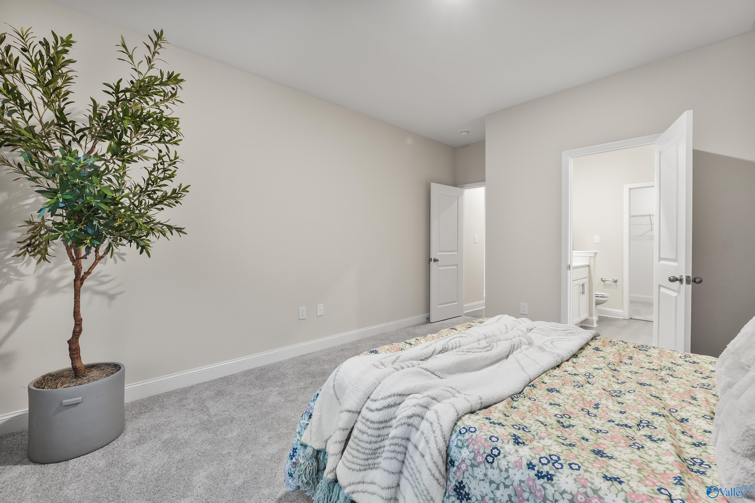 Master bedroom with floral bedding, potted tree, and open en-suite bath in Davidson Homes The Asheville C, Huntsville AL