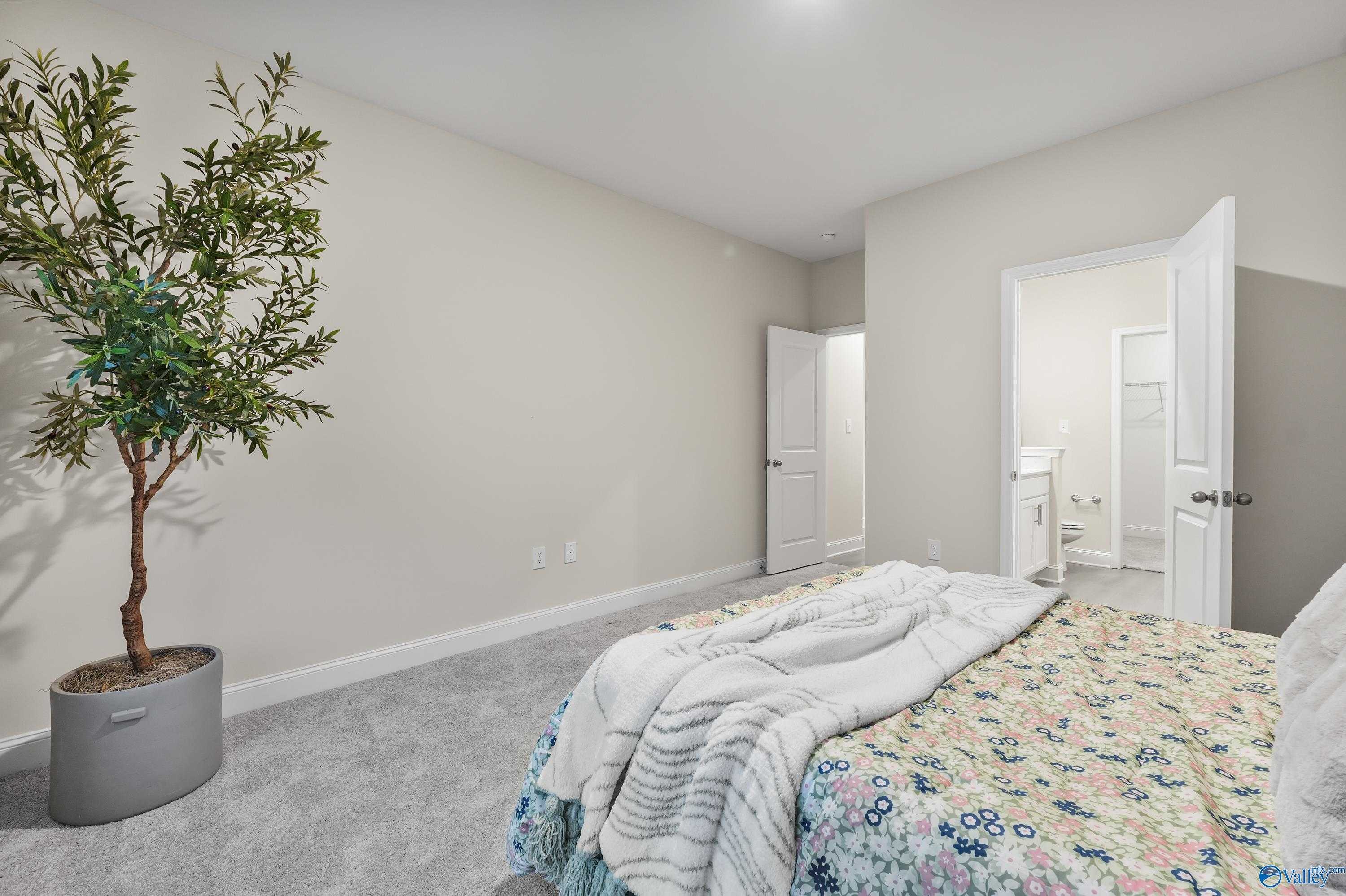 Cozy bedroom with floral bedding, potted tree, and en-suite bathroom in The Asheville C by Davidson Homes, Huntsville AL