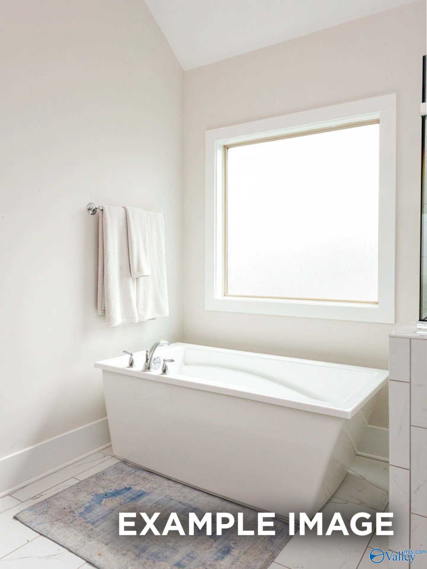 Elegant master bathroom featuring freestanding soaking tub, frosted window, and plush towels in Davidson Homes The Finleigh, Meridianville, Alabama