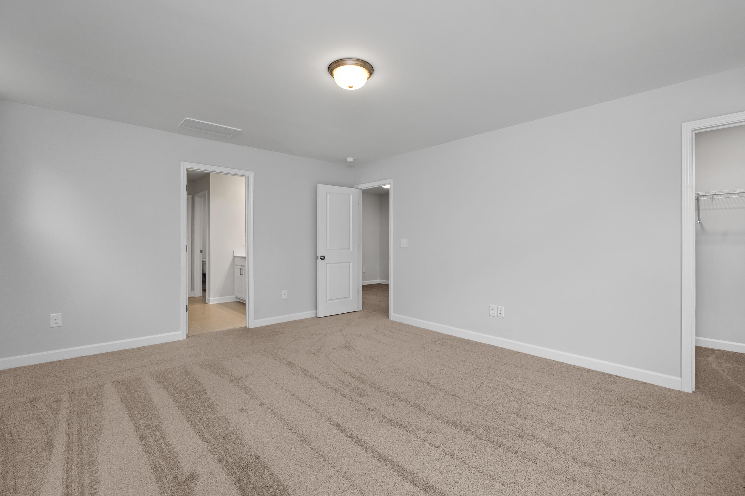 Spacious upper-floor master suite in The Durham featuring plush carpeting, walk-in closet, and private bathroom access.