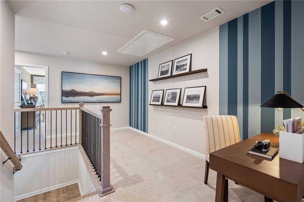 Elegant upstairs home office with blue striped accent wall, wooden desk, framed seascape art, and staircase in Davidson Homes The Marion C, Winder, GA