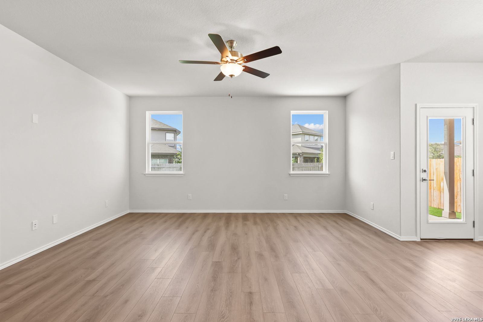 Bright open living area with wood-look flooring, ceiling fan, and glass-paneled back door in The Daphne I, Bricewood, San Antonio