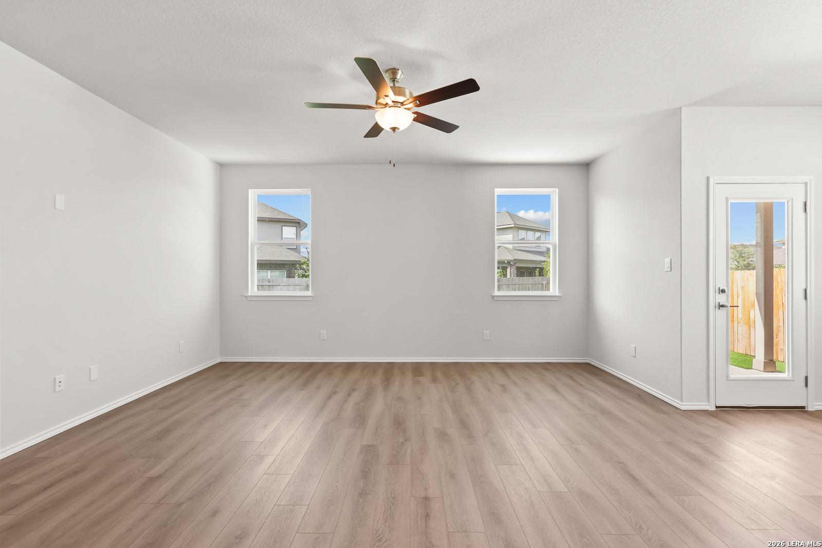 Bright open living area with wood-look flooring, ceiling fan, and glass-paneled back door in The Daphne I, Bricewood, San Antonio
