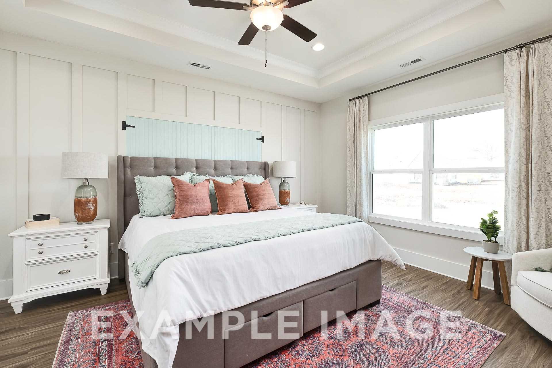Spacious master bedroom in The Everett B with tufted gray headboard, ceiling fan, large windows, and neutral decor