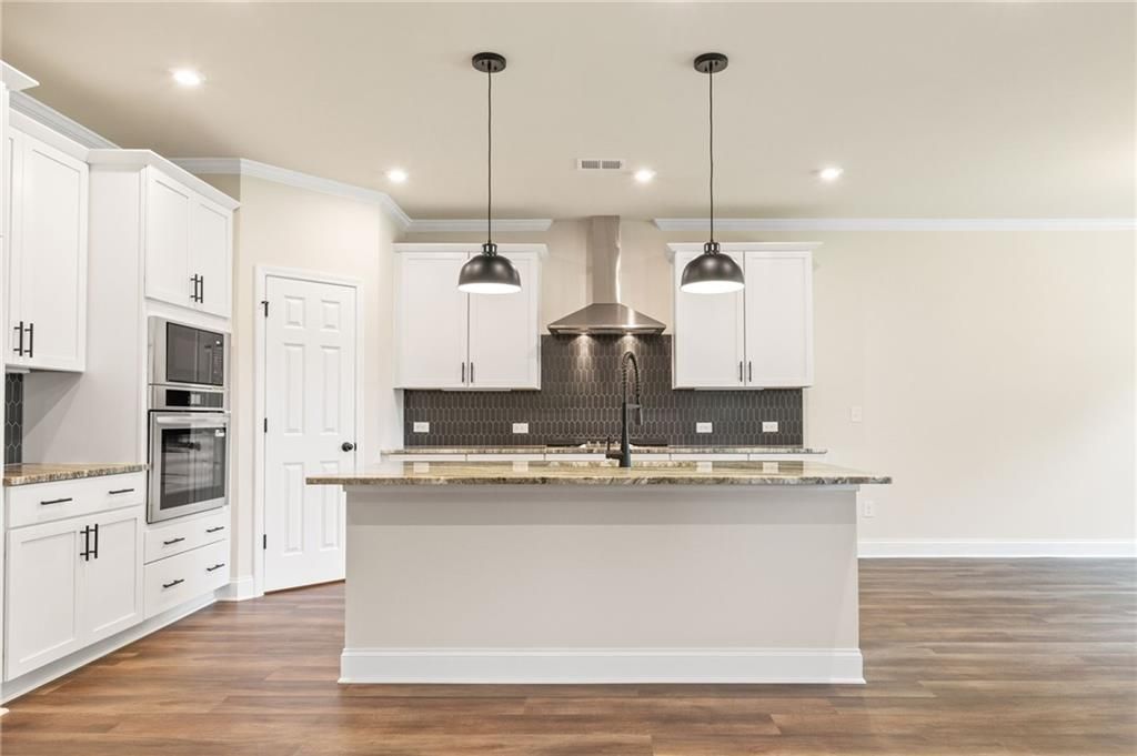 Modern white kitchen featuring large island, stainless steel appliances, subway tile backsplash, and hardwood floors in The Harrison H, Winder GA