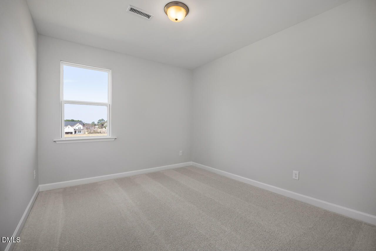 Bright empty secondary bedroom with beige carpet, gray walls, and large window in Davidson Homes The Willow G, Angier, NC
