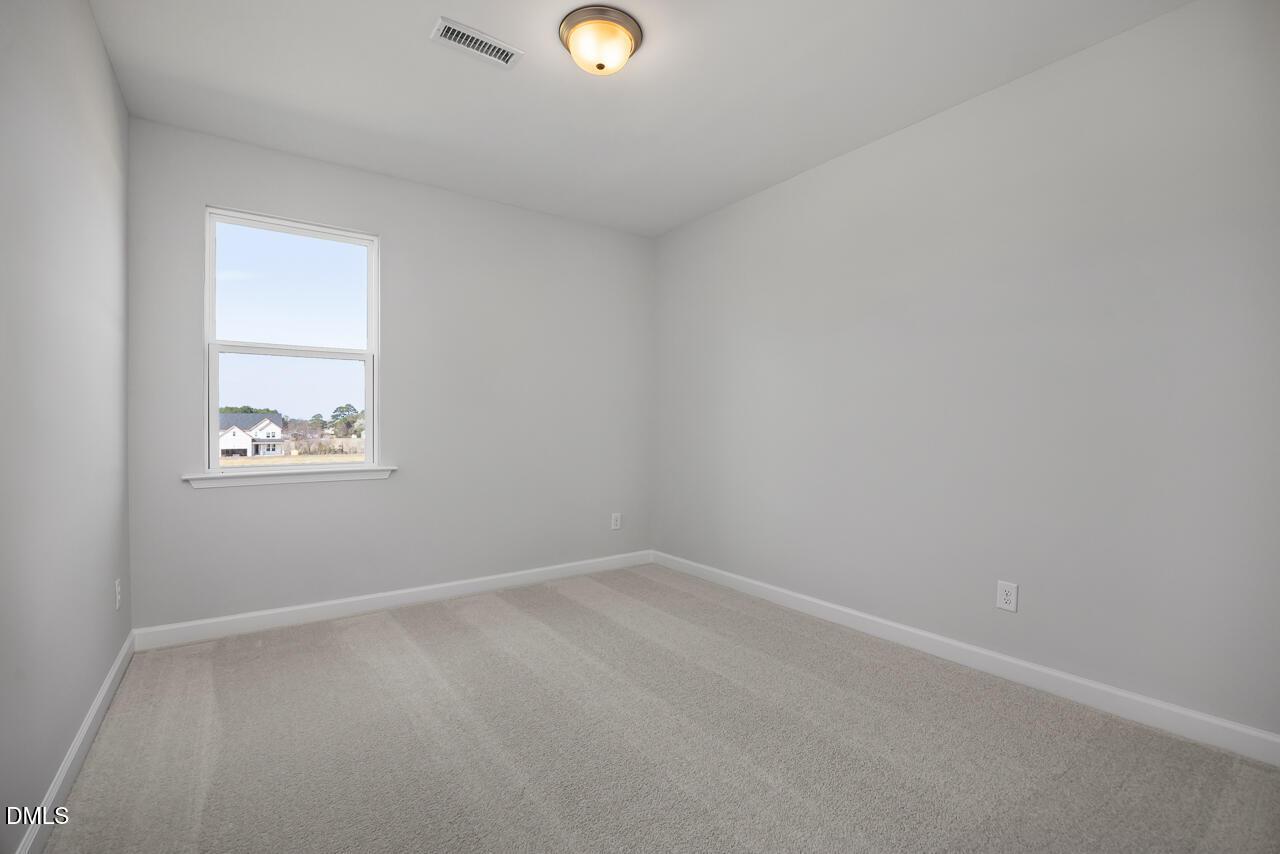 Bright empty secondary bedroom with beige carpet, gray walls, and large window in Davidson Homes The Willow G, Angier, NC