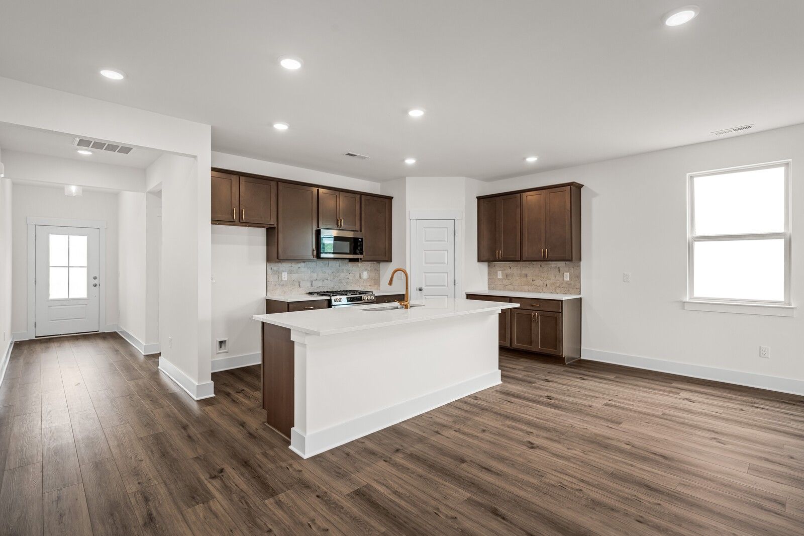 Open-concept kitchen with white quartz island, dark cabinets, and wood flooring in Prairie C plan at Woods Crossing, Gallatin.