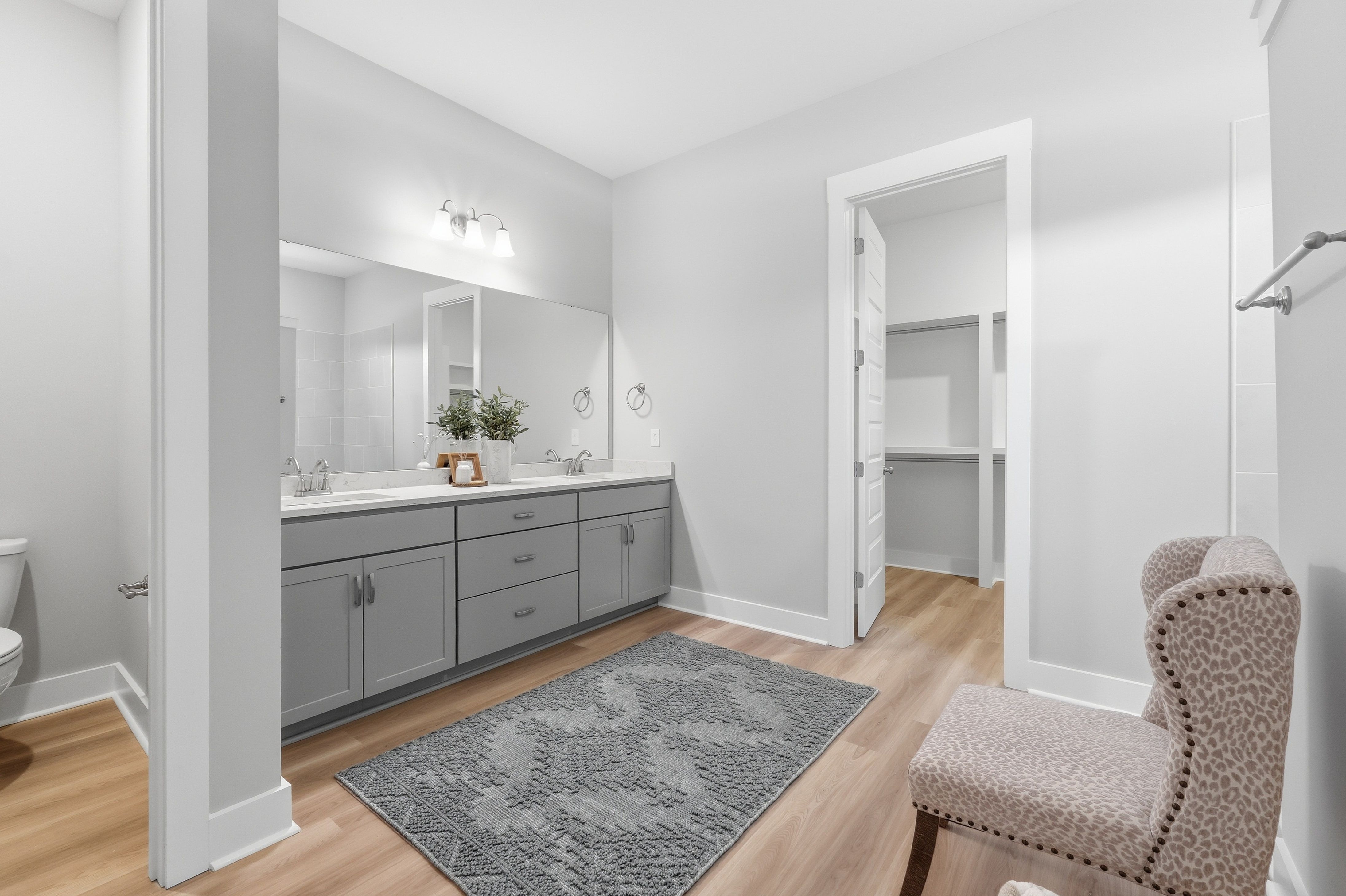 Spacious primary bathroom at The Meadows at Hampton Cove in Owens Cross Roads AL with double gray vanity, mirror, toilet, and hardwood floors
