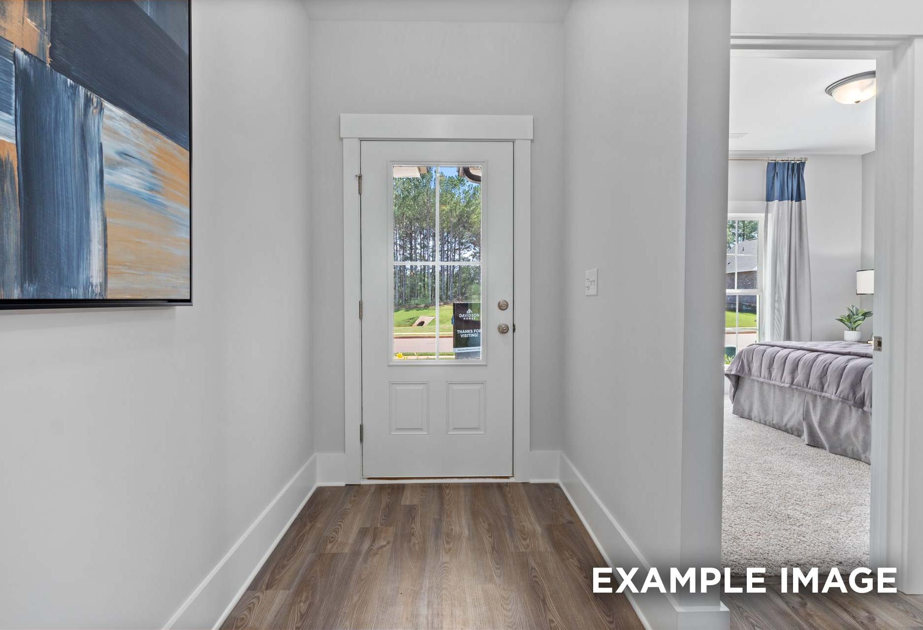 Hallway to master suite in The Franklin C home with glass-paneled door, hardwood floors, abstract art, and bedroom glimpse