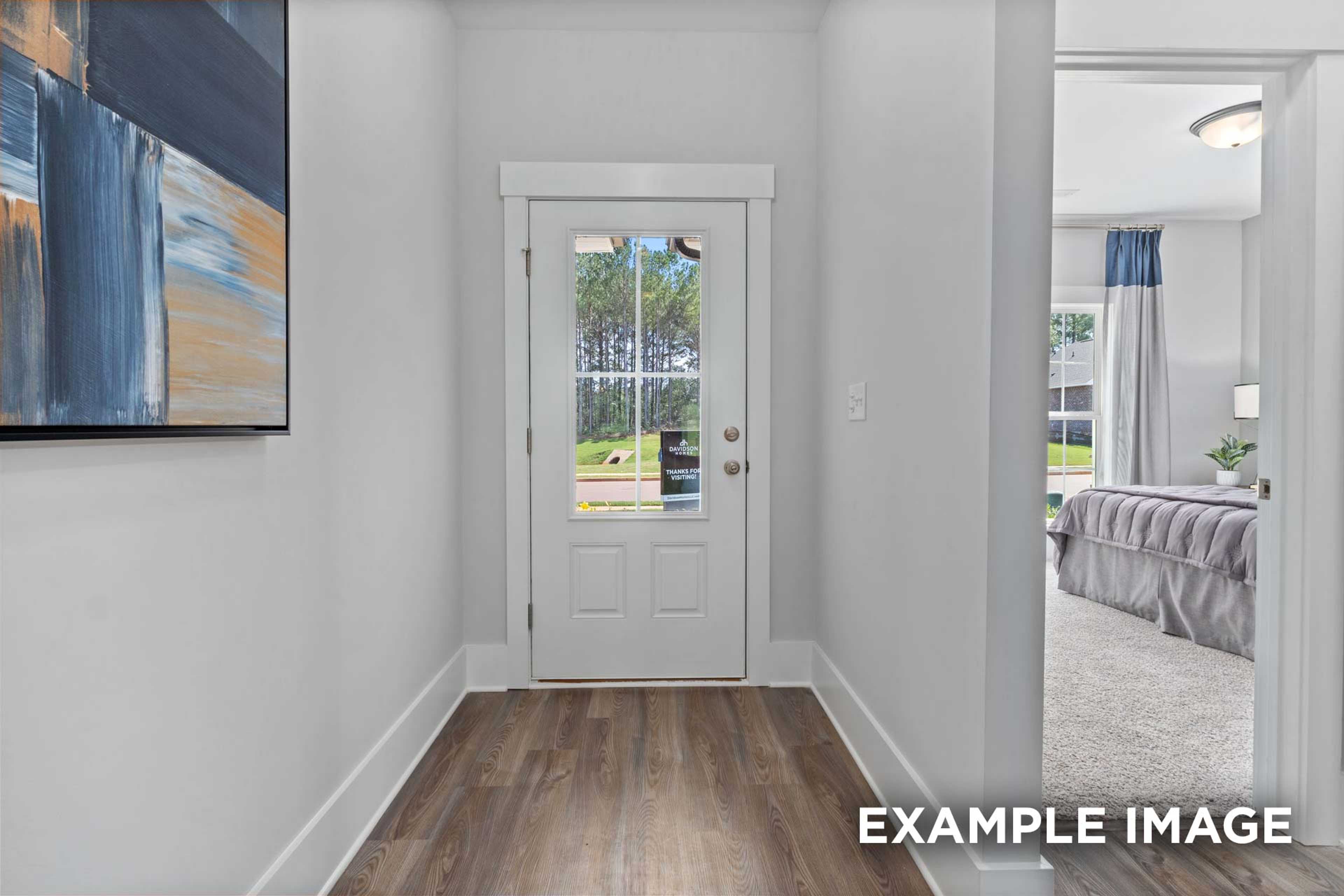 Hallway to master suite in The Franklin C home with glass-paneled door, hardwood floors, abstract art, and bedroom glimpse