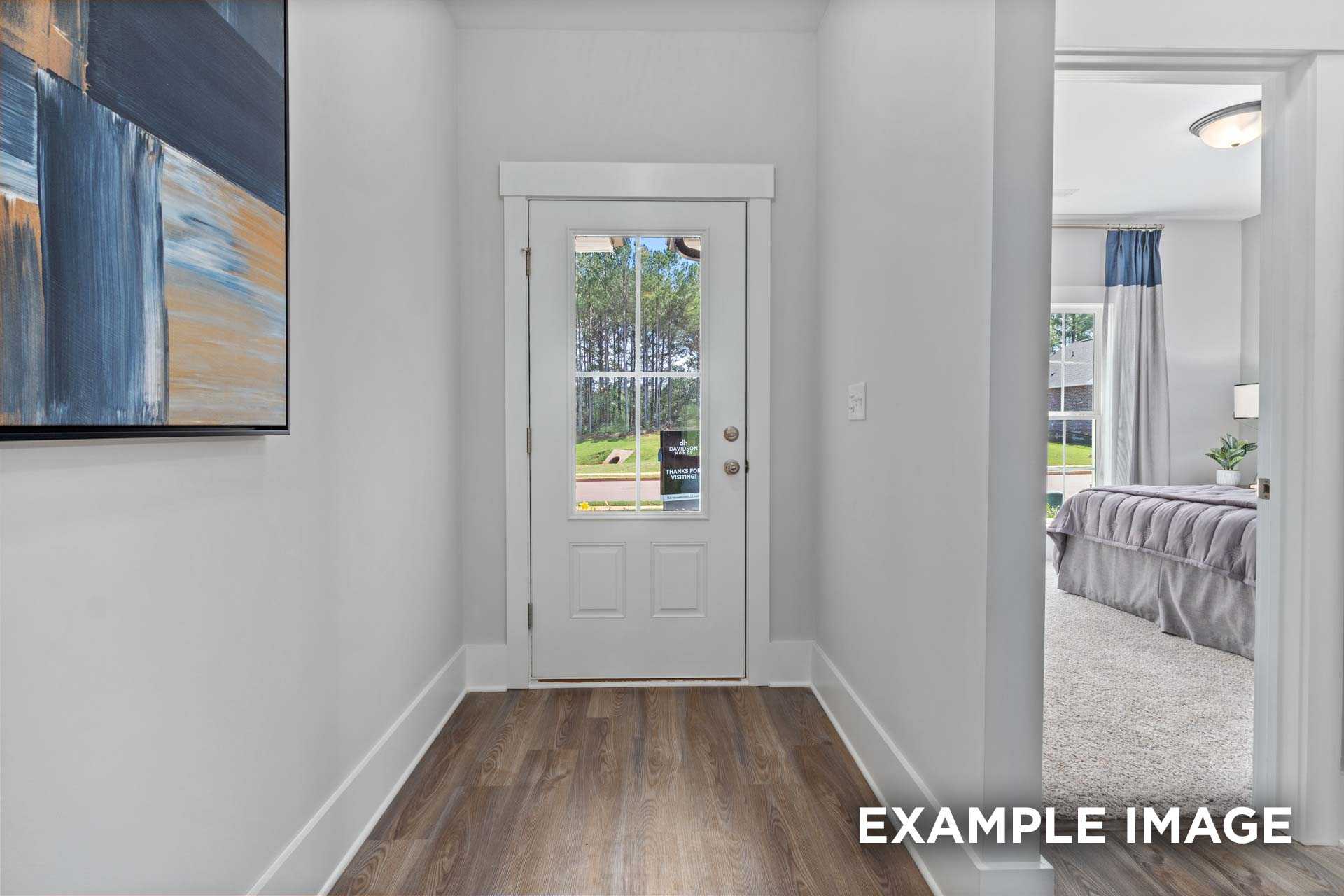 Hallway to master suite in The Franklin C home with glass-paneled door, hardwood floors, abstract art, and bedroom glimpse
