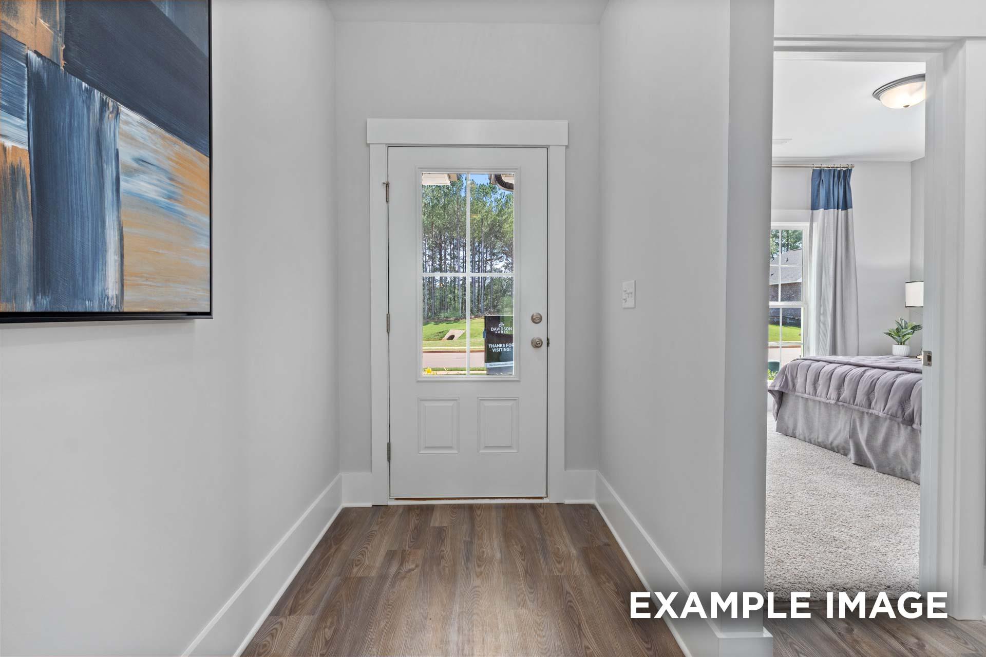 Hallway to master suite in The Franklin C home with glass-paneled door, hardwood floors, abstract art, and bedroom glimpse