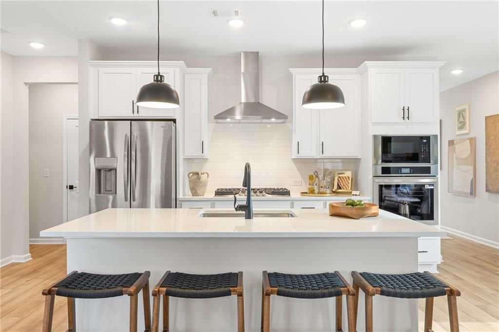Modern white kitchen with quartz island, stainless steel appliances, and pendant lighting in The Rabun B, Canton, Georgia.