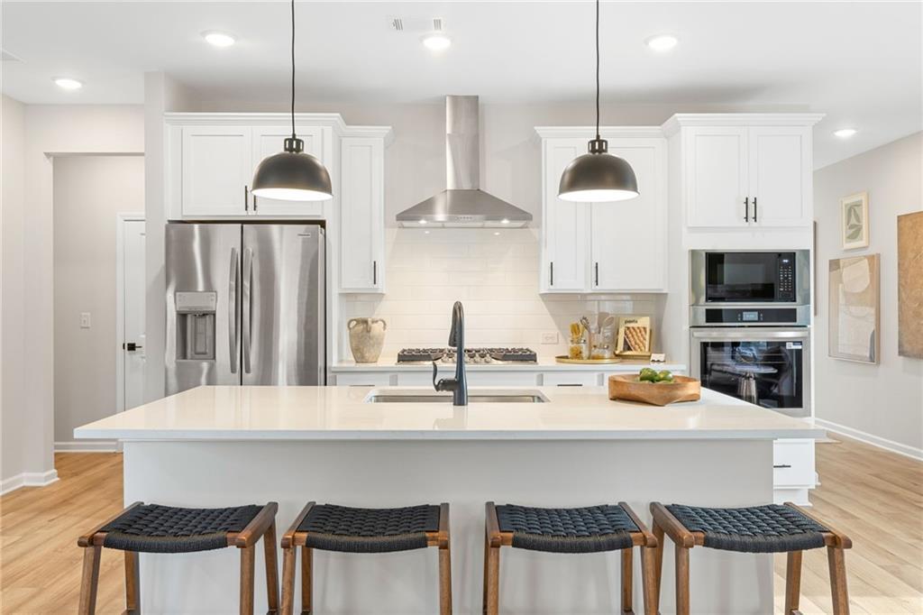 Modern white kitchen with quartz island, stainless steel appliances, and pendant lighting in The Rabun B, Canton, Georgia.