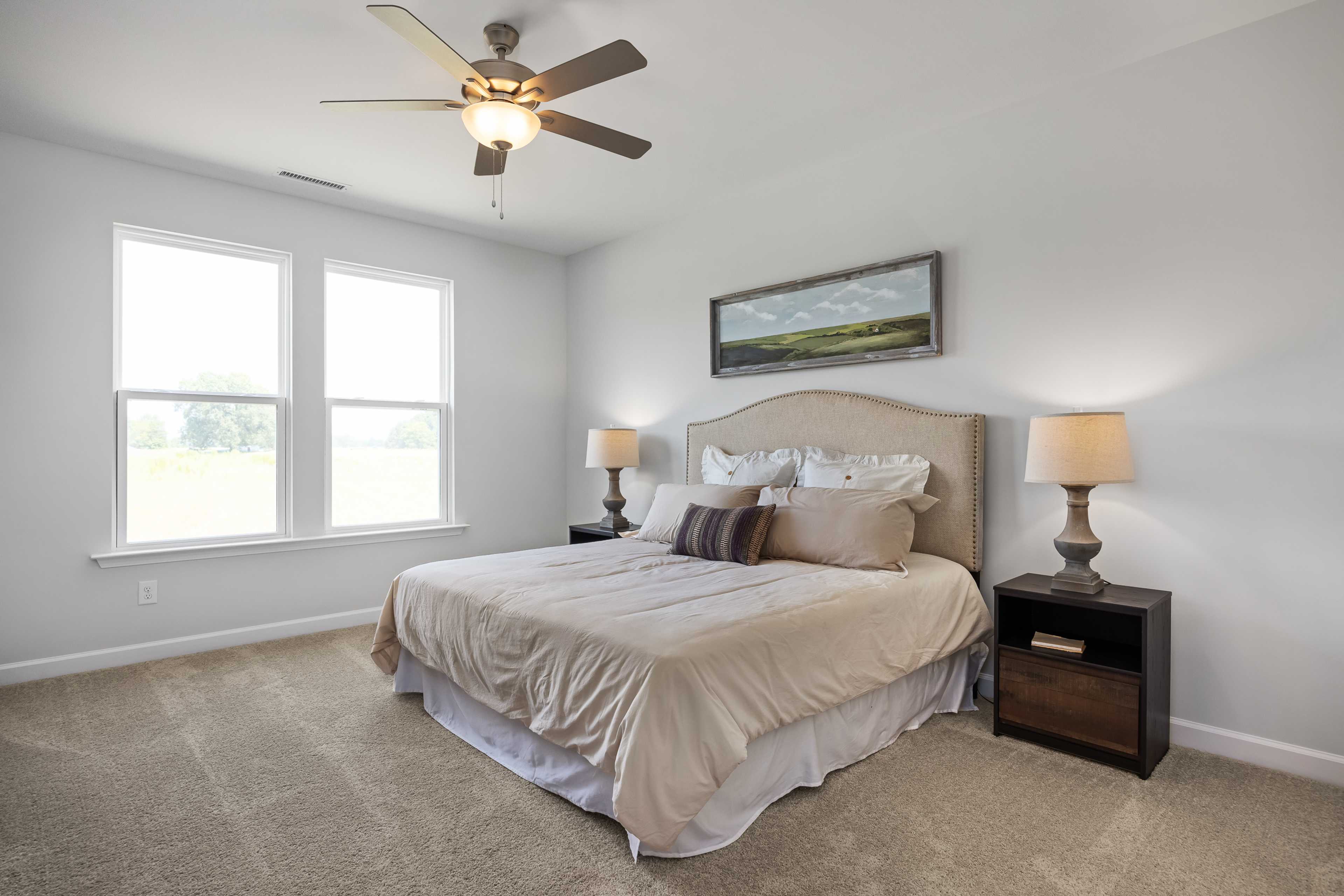 Spacious master bedroom at Woodland Crossing in Zebulon NC by Davidson Homes with king bed, tufted headboard, lamps, and large windows