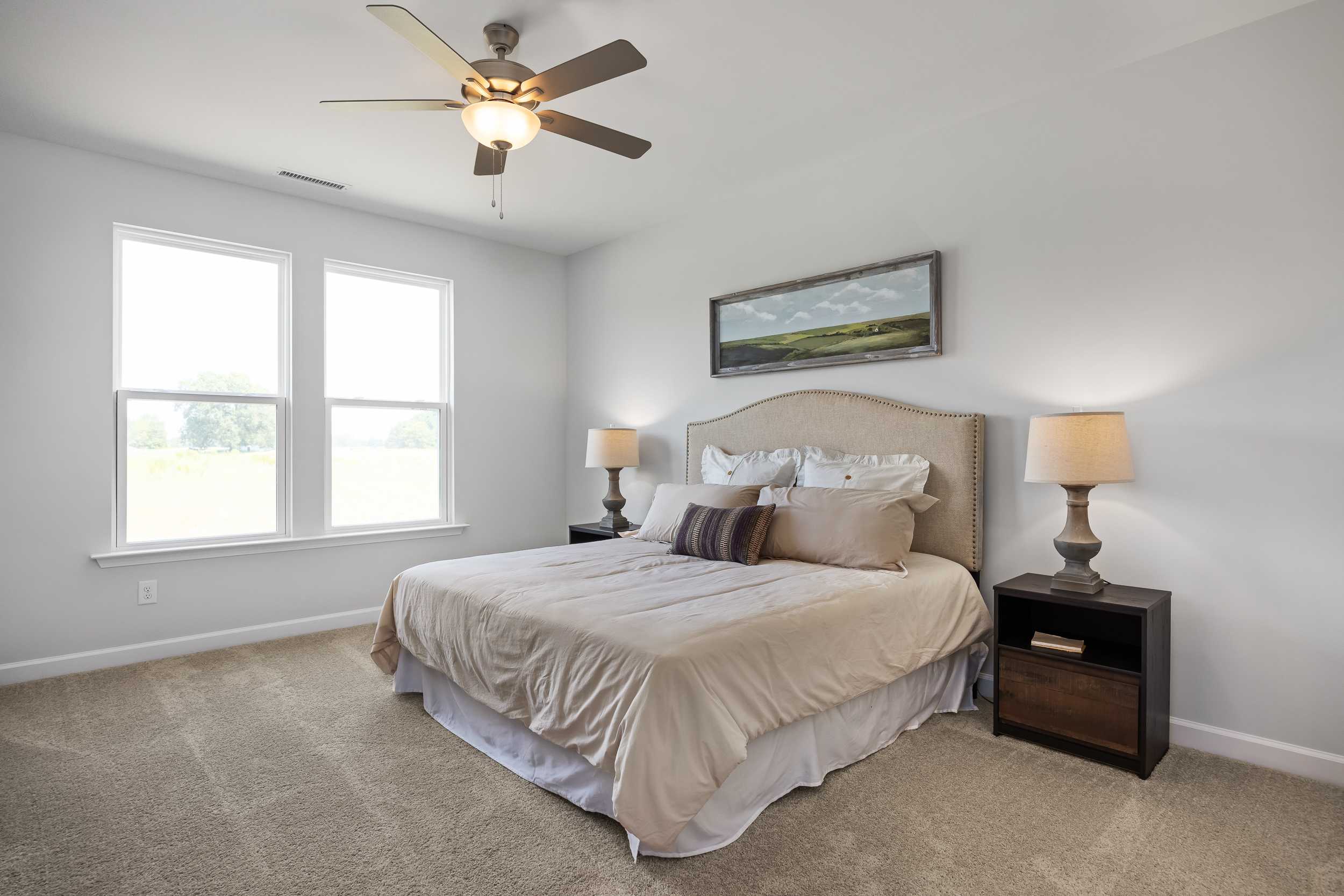 Spacious master bedroom in The Daphne C with king bed, upholstered headboard, lamps, ceiling fan, and large windows