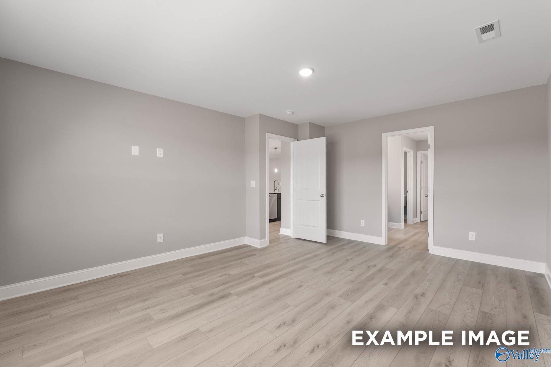 Spacious empty bedroom with light gray walls, oak laminate floors, open doors to bathroom and utility in Everett B home, Toney AL