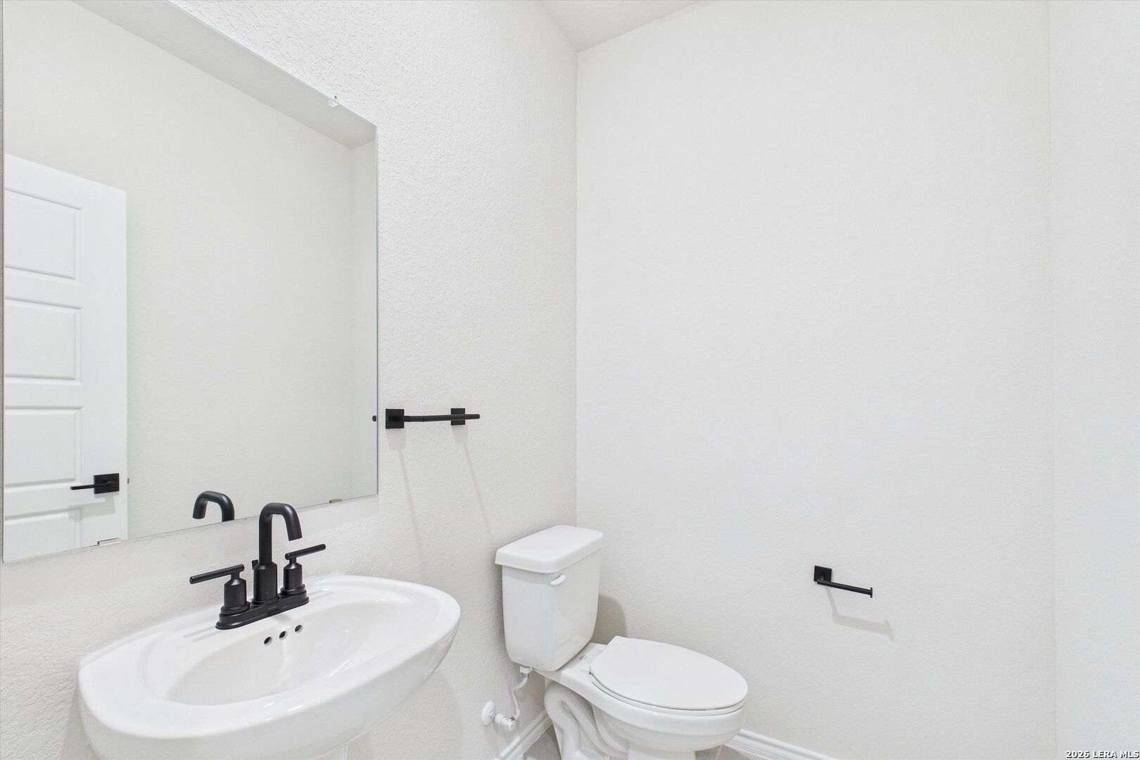Bright white powder room with black faucet, vanity sink, and toilet in Davidson Homes The Gillian B, San Antonio, Texas
