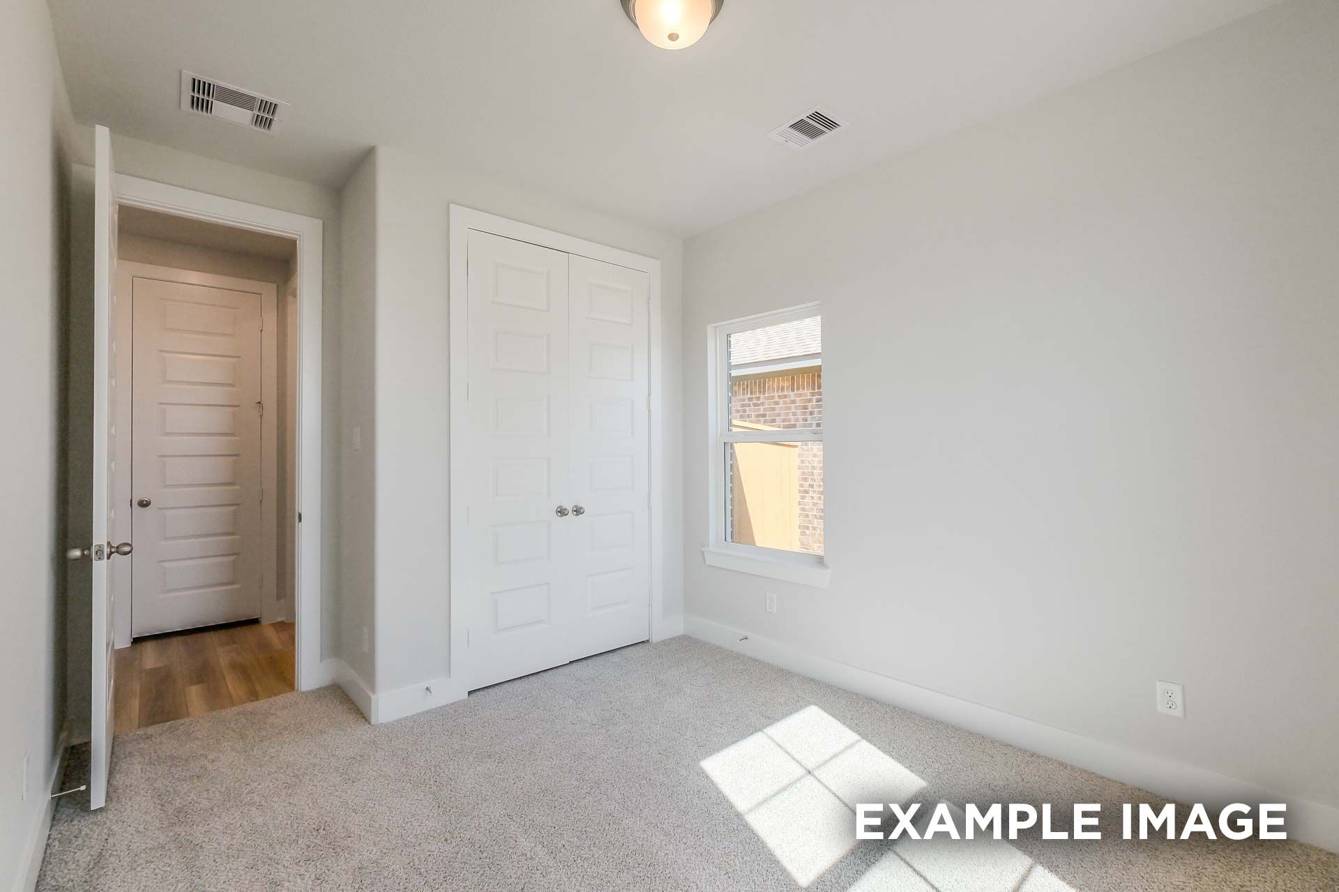 Bright secondary bedroom in The Luna K with open closet door, double bi-fold doors, large window, and gray carpet