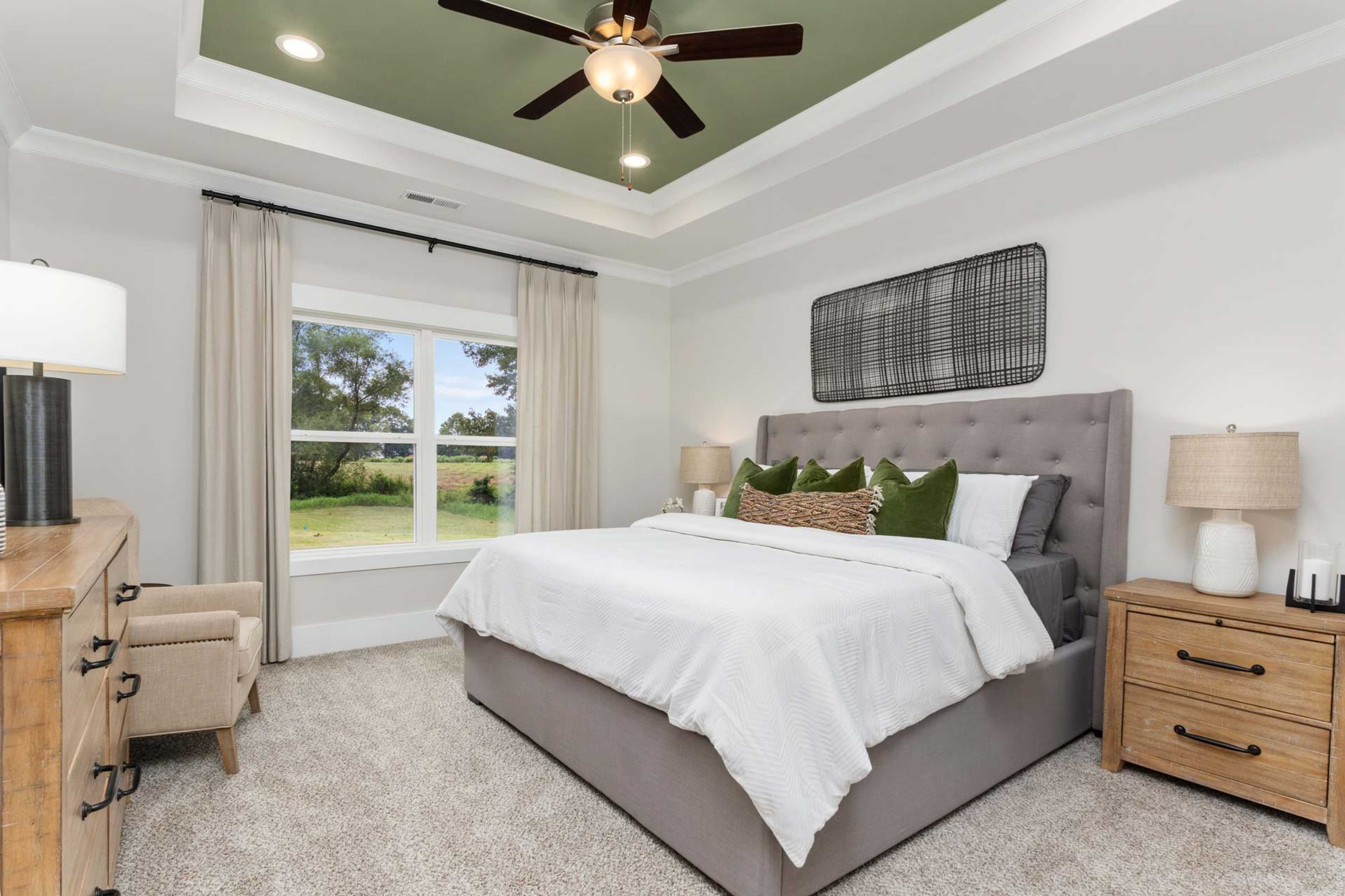 Spacious master bedroom at The Meadows in Athens Alabama with white bed green pillows and garden view