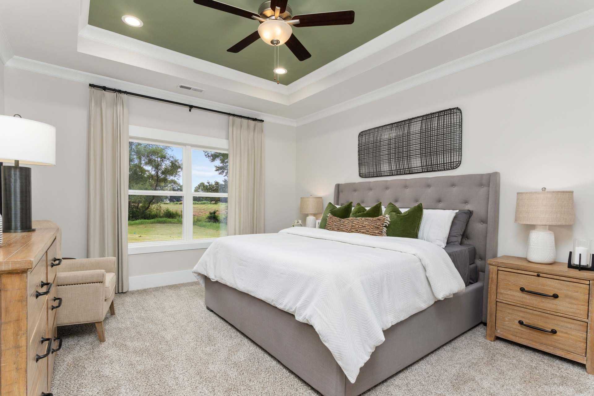 Spacious master bedroom at The Meadows in Athens Alabama with white bed green pillows and garden view