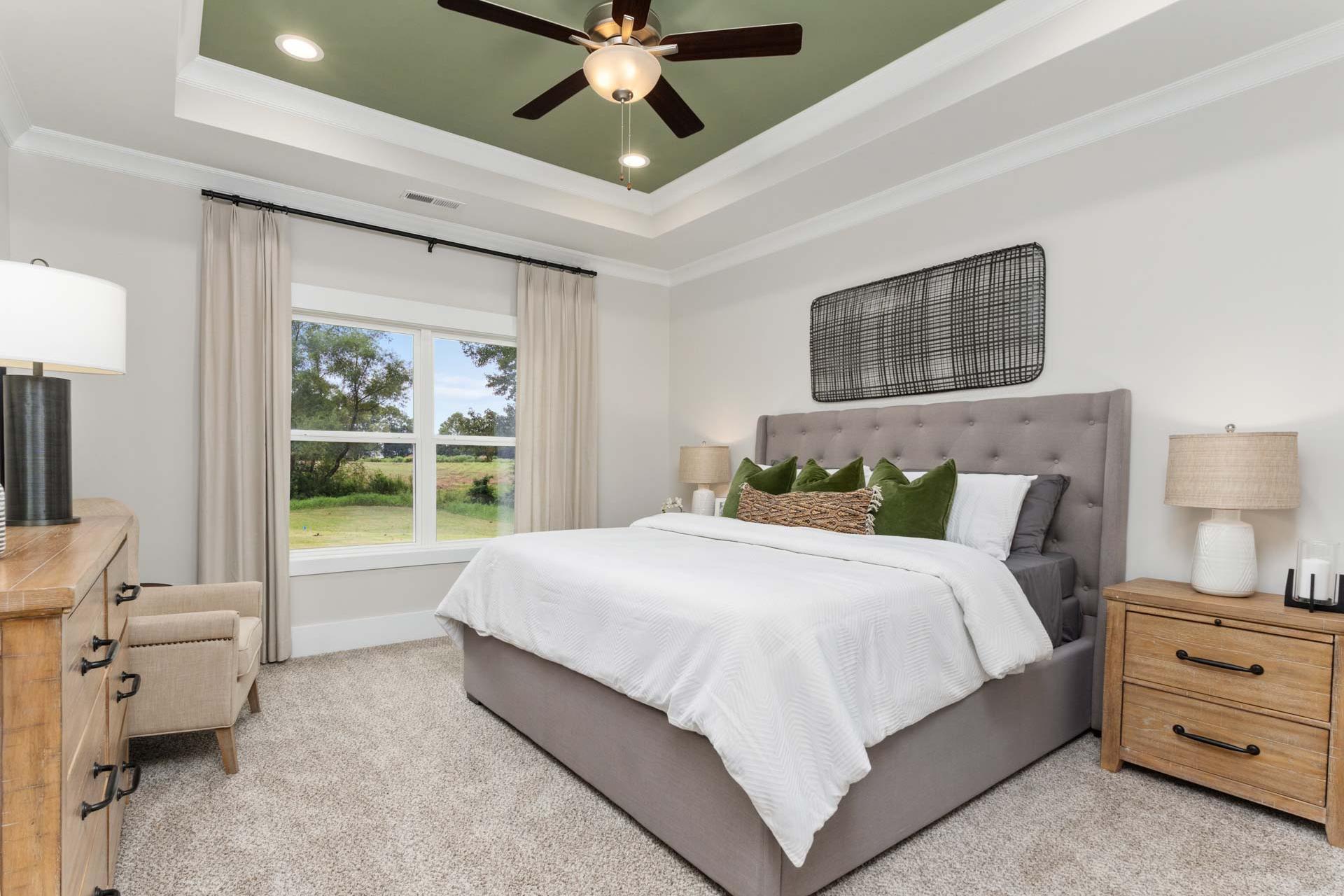 Spacious master bedroom at The Meadows in Athens Alabama with white bed green pillows and garden view