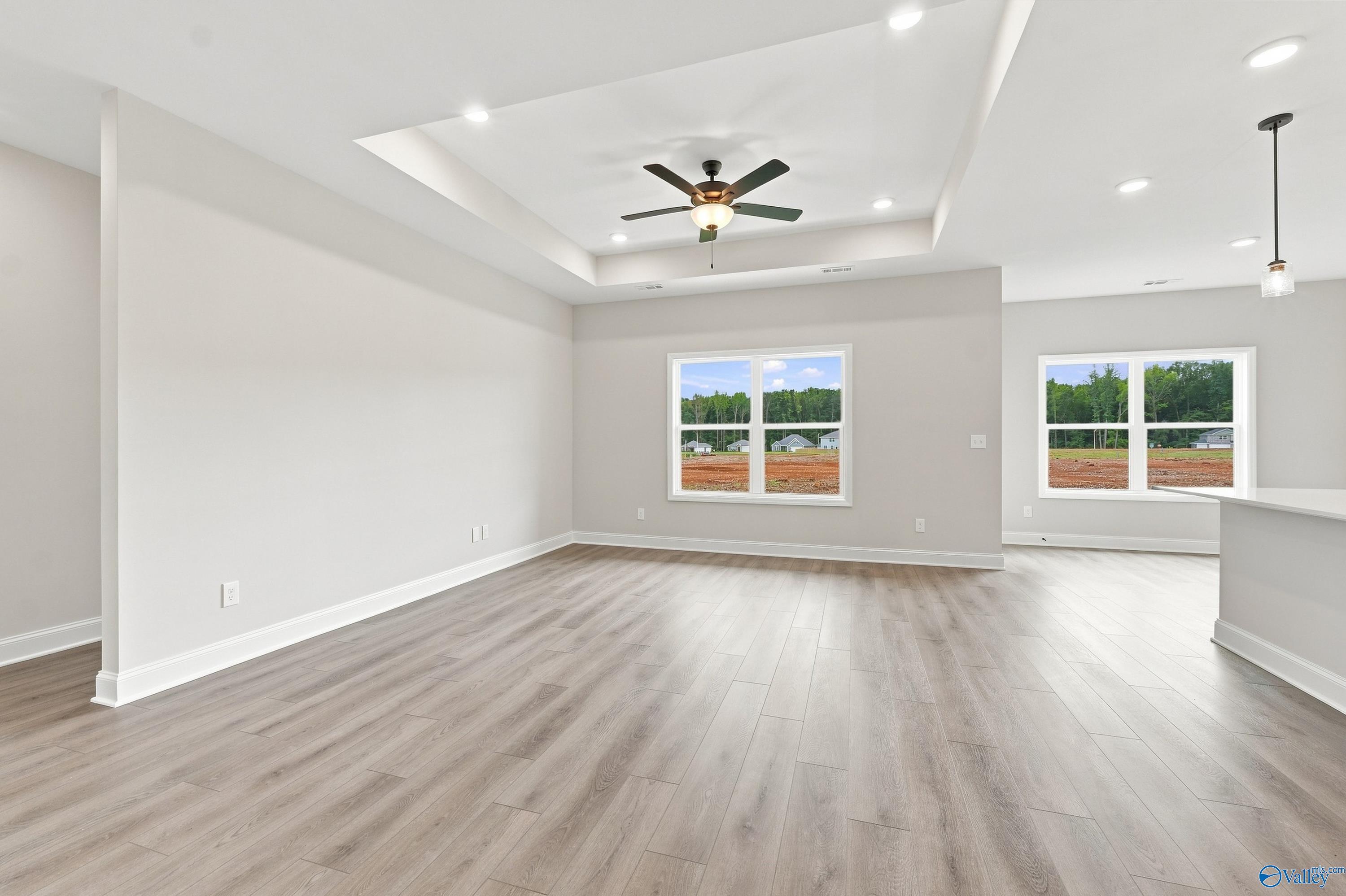 Open-concept living area with luxury vinyl plank flooring, tray ceiling, and ceiling fan in Davidson Homes The Asheville E floor plan