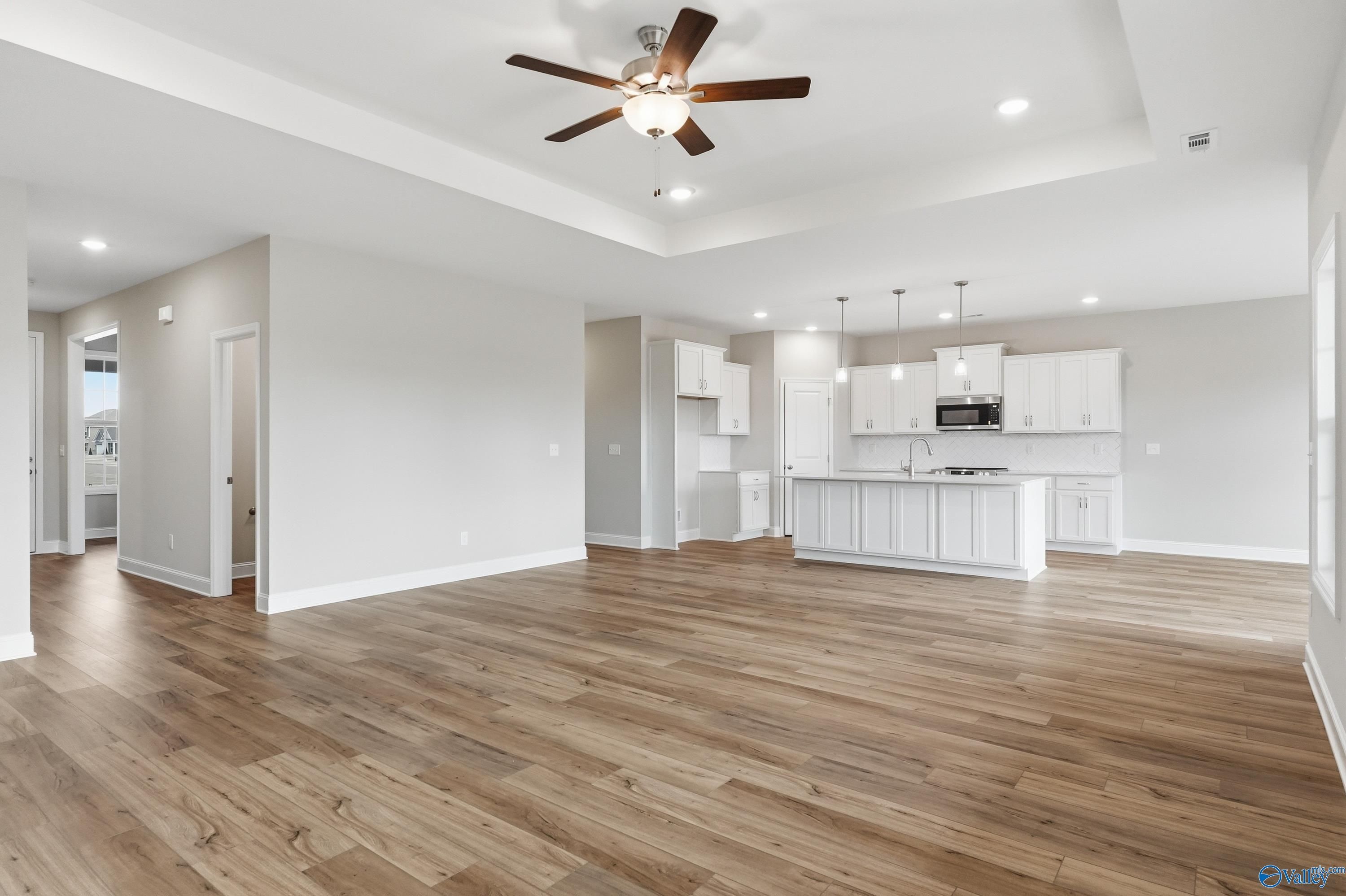 Open-concept kitchen and living area with white cabinets, hardwood floors, and ceiling fan in Davidson Homes The Rockford, Meridianville, Alabama