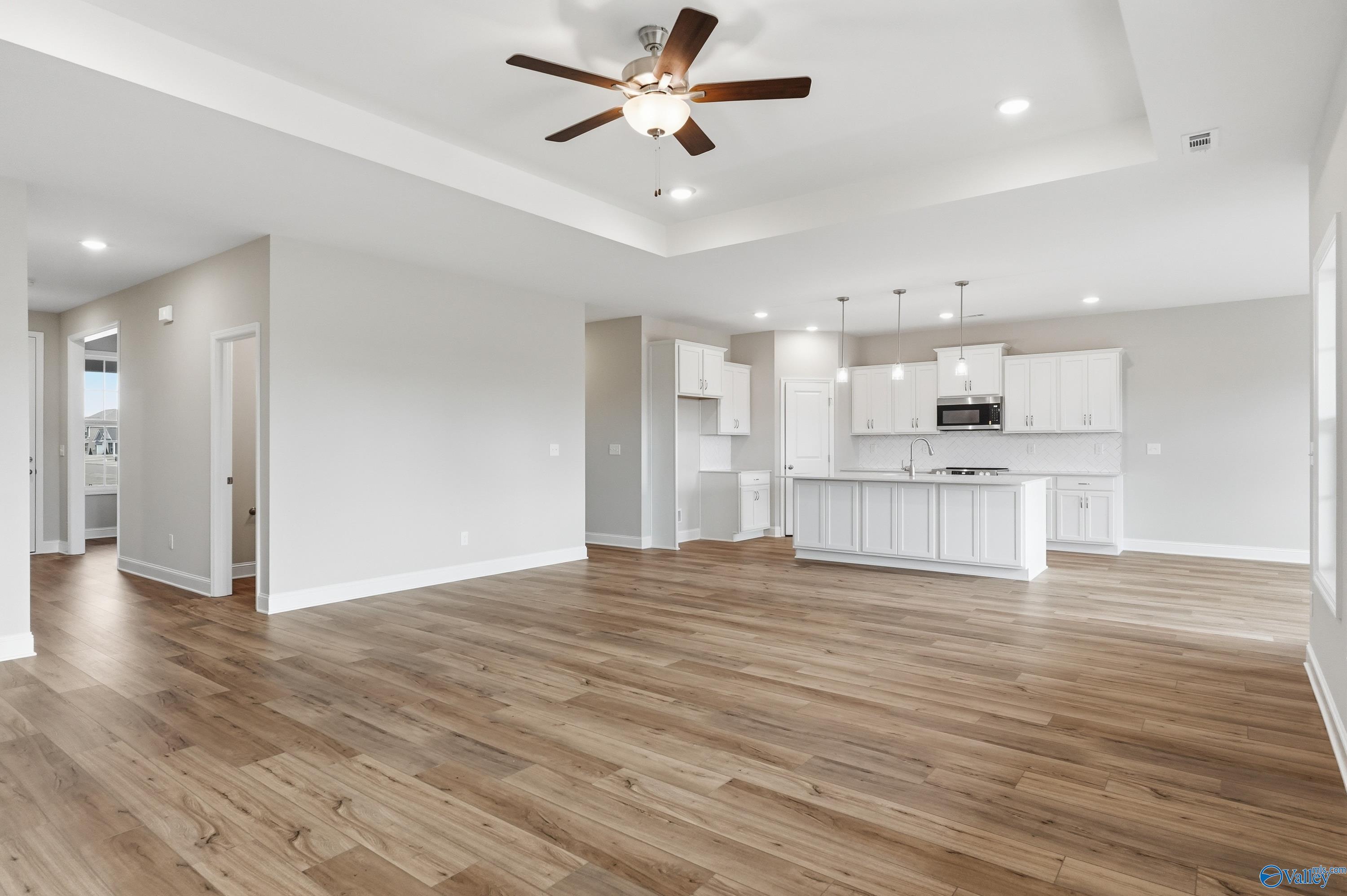Open-concept kitchen and living area with white cabinets, hardwood floors, and ceiling fan in Davidson Homes The Rockford, Meridianville, Alabama